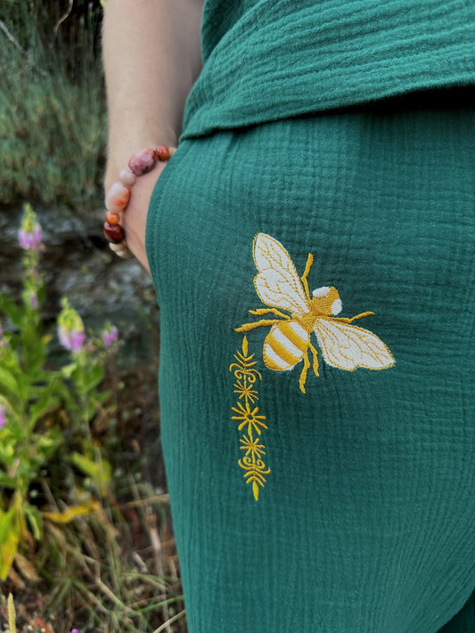 Green garment with a yellow bee design embroidered on it, held by a person in a natural setting.