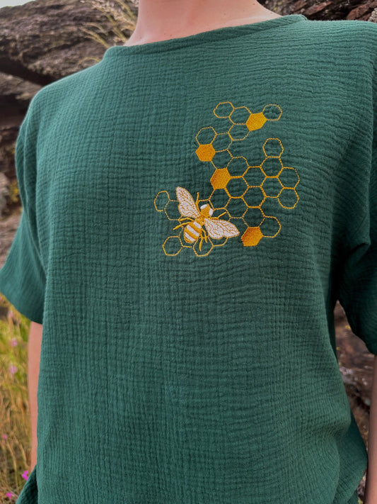 Green shirt with embroidered bee and honeycomb design worn by a person outdoors.