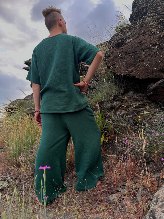 Person wearing a green outfit standing on a rocky landscape with grass and flowers.