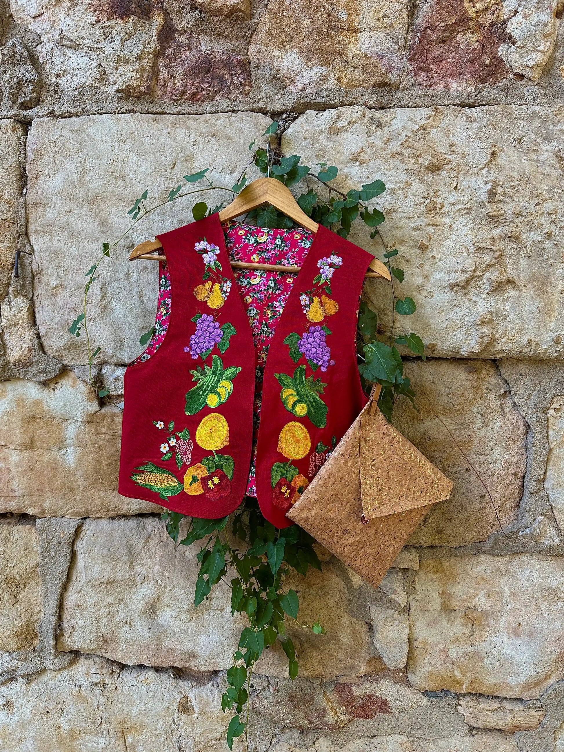 Red embroidered vest with fruit patterns hanging on a stone wall