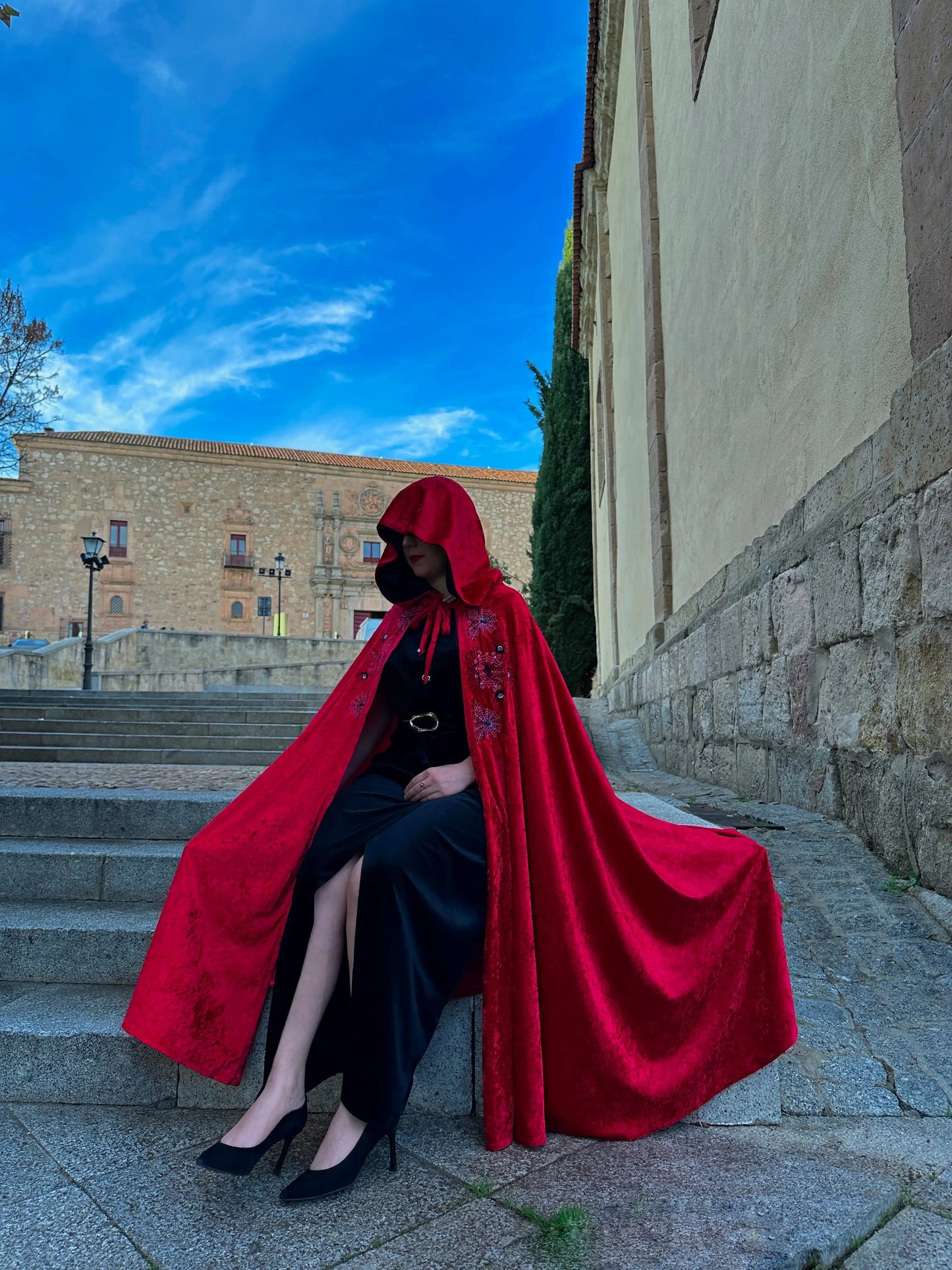 Person wearing a red cloak sitting on stone steps with a building in the background