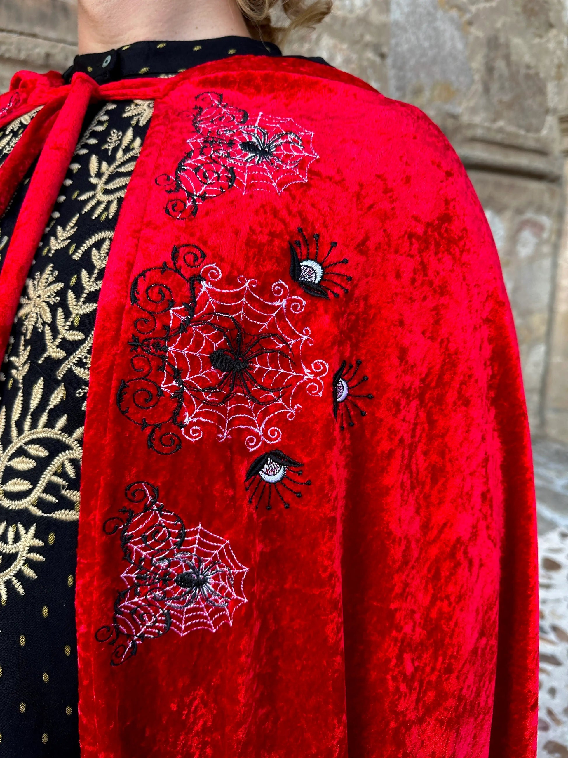 Red garment with spider web and eye embroidery against a stone wall background