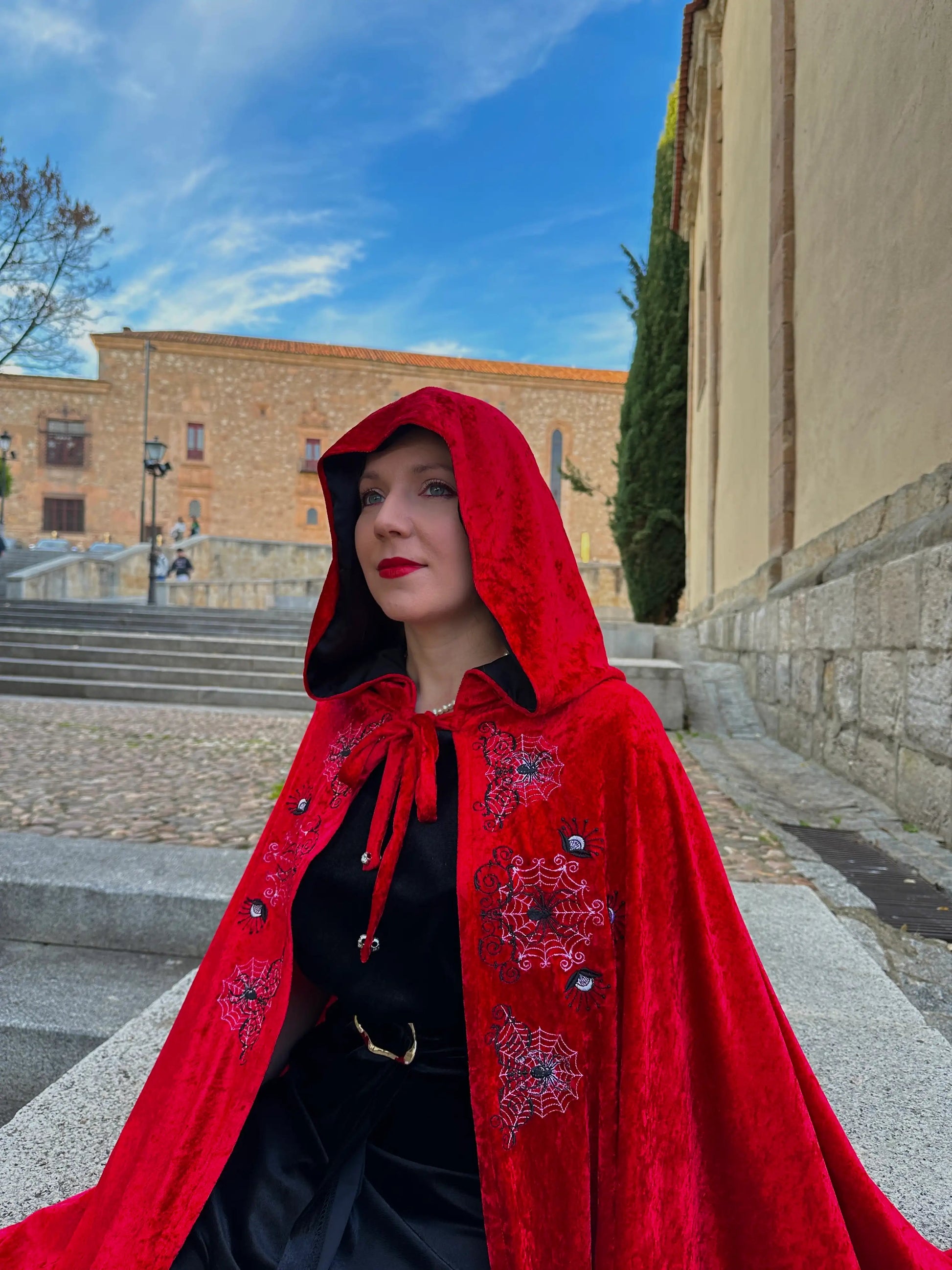 Person wearing a red hooded cloak with floral embroidery in an outdoor setting.