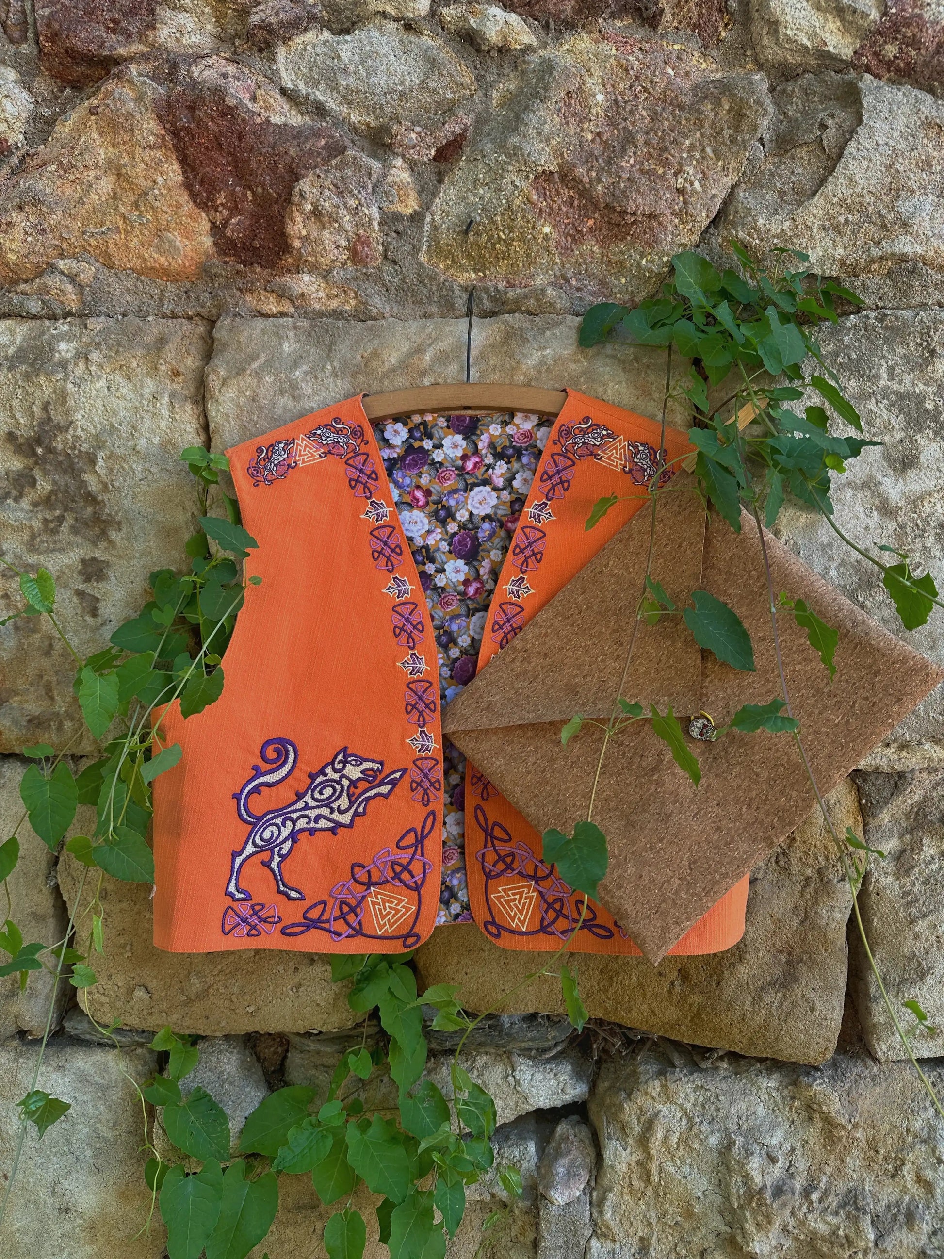 Orange fabric with floral pattern and embroidered design against a stone wall.