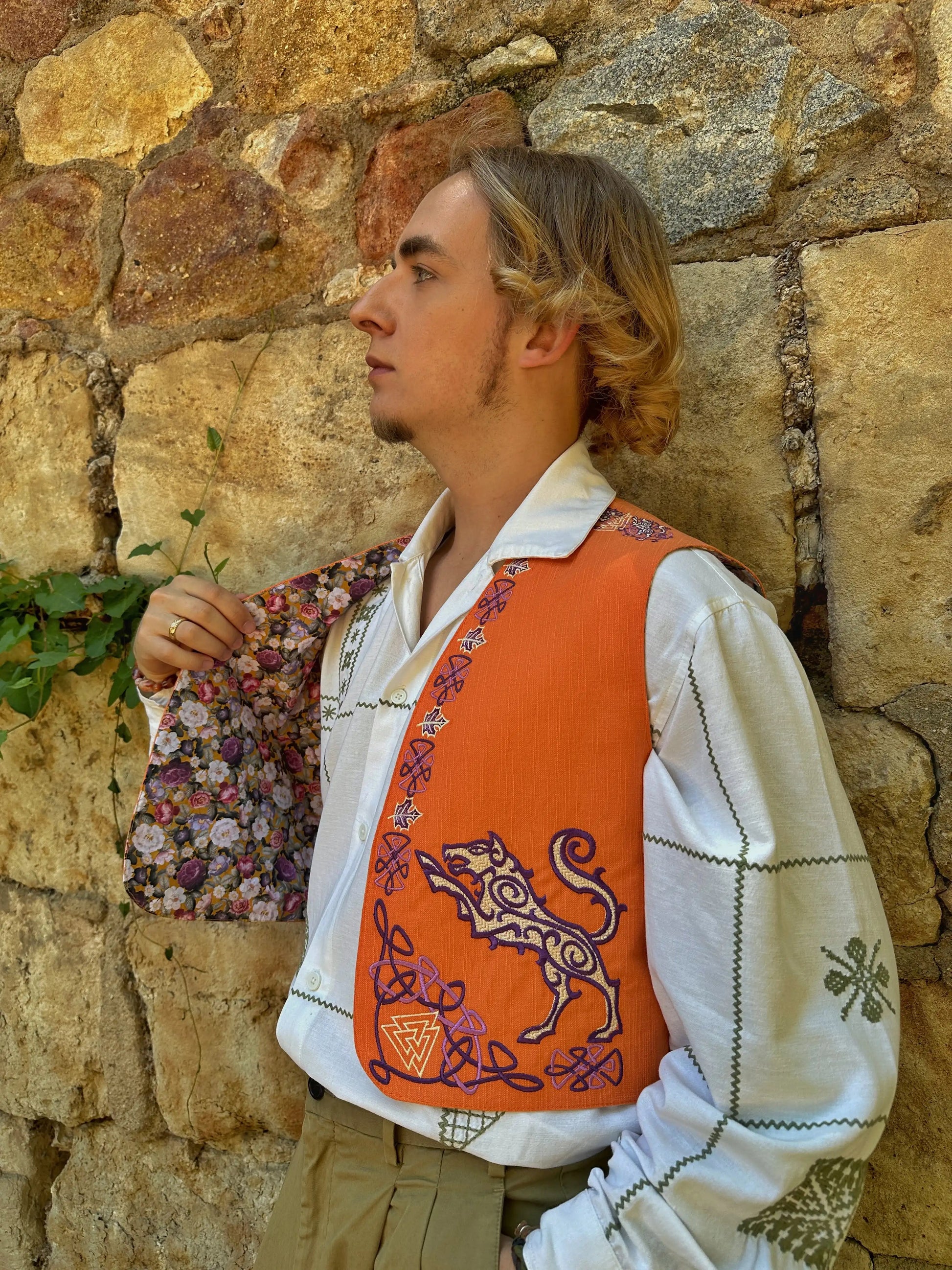 Person wearing a white shirt with an orange vest featuring a tiger design, standing against a stone wall.