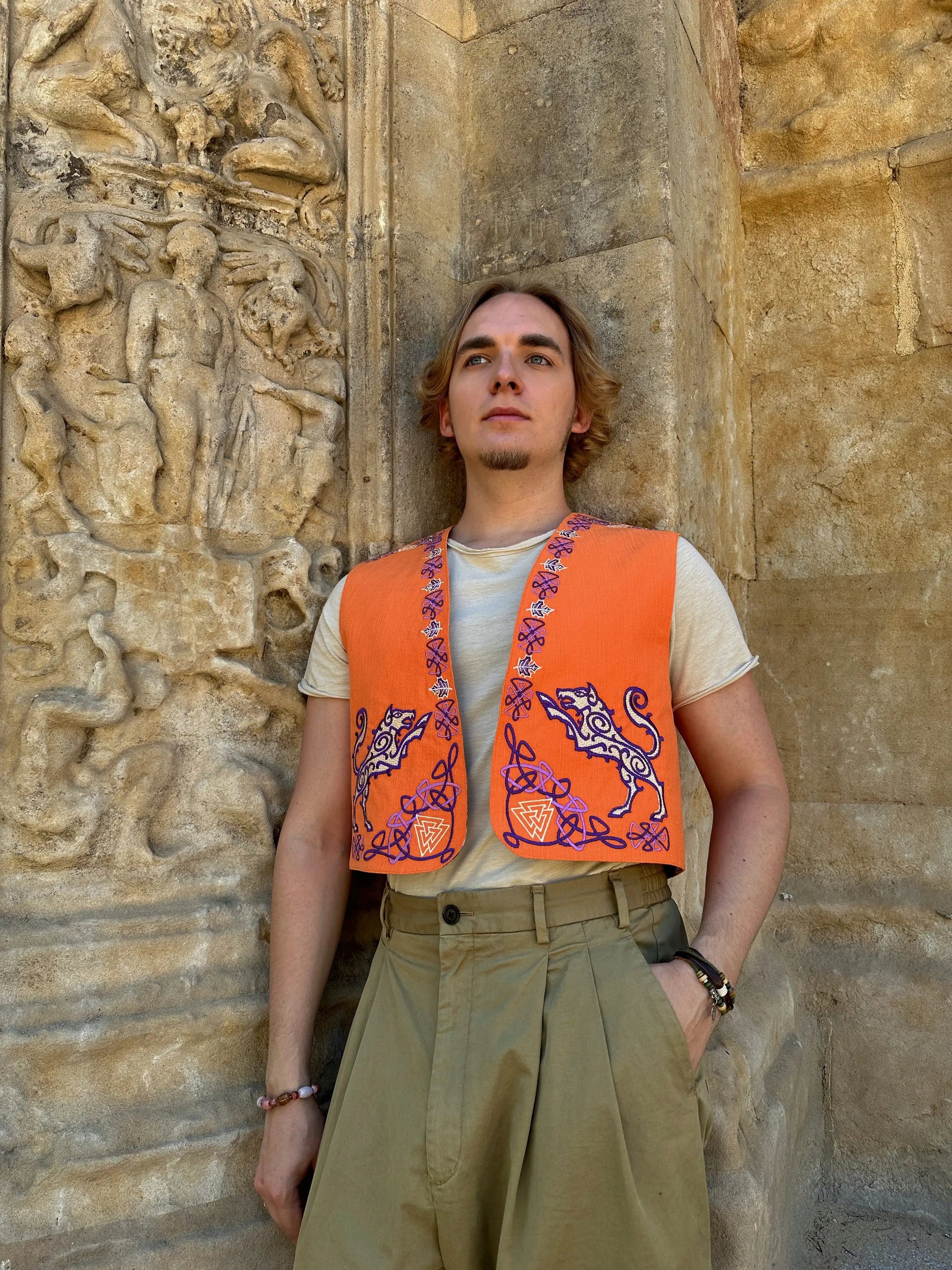 Person wearing an orange vest with purple designs against a stone wall.