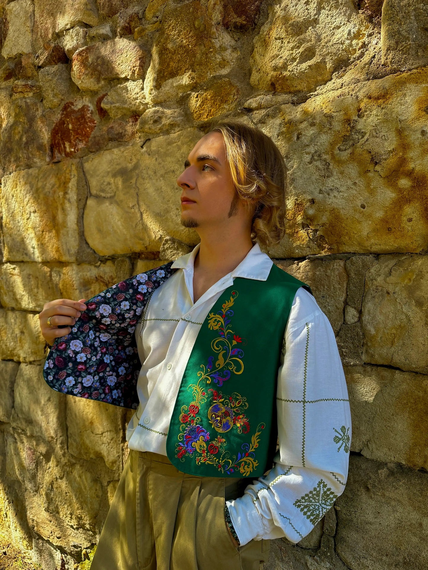 Man in historical costume holding a floral handkerchief against a stone wall