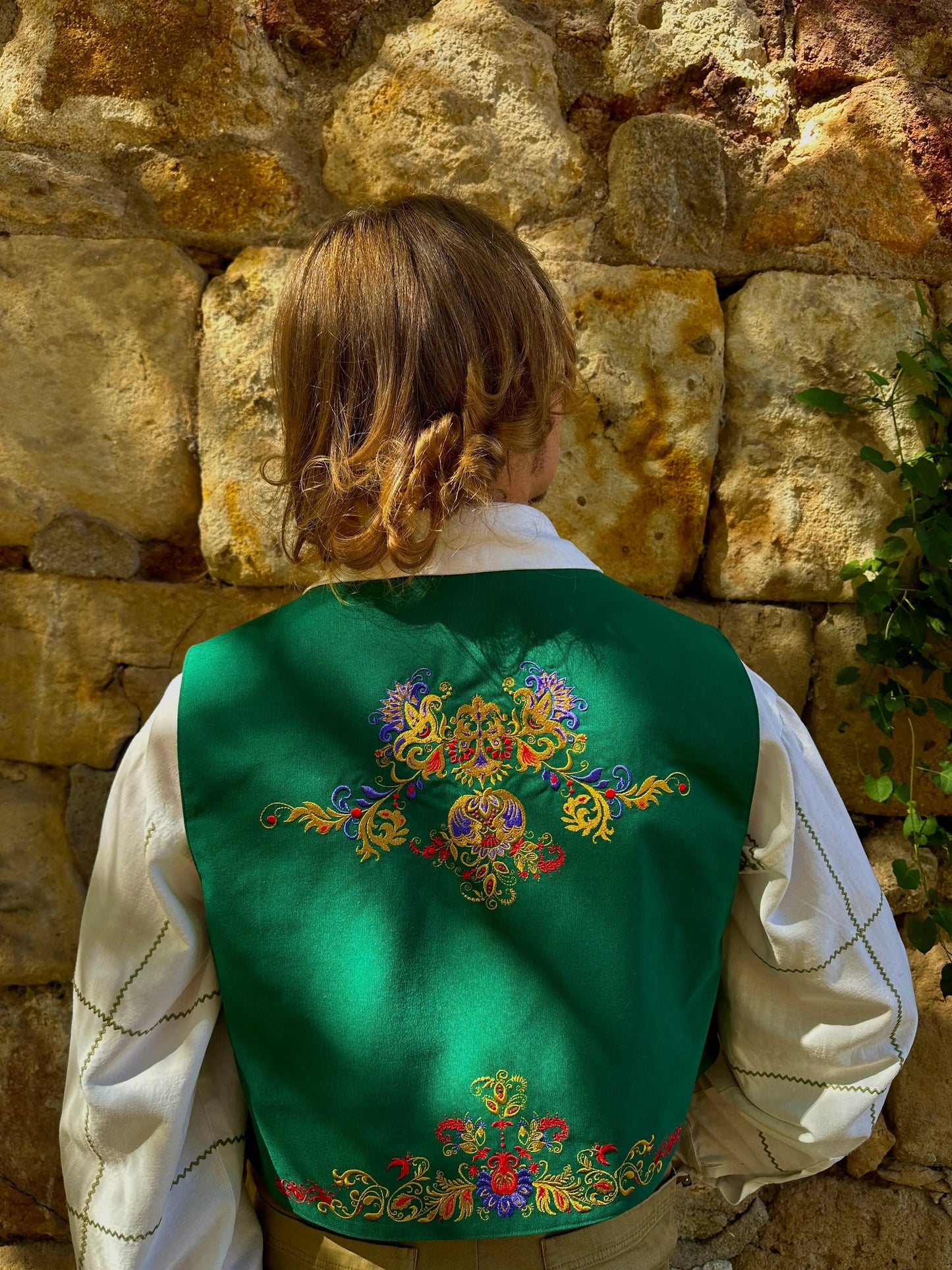 Person wearing a green embroidered vest against a stone wall.