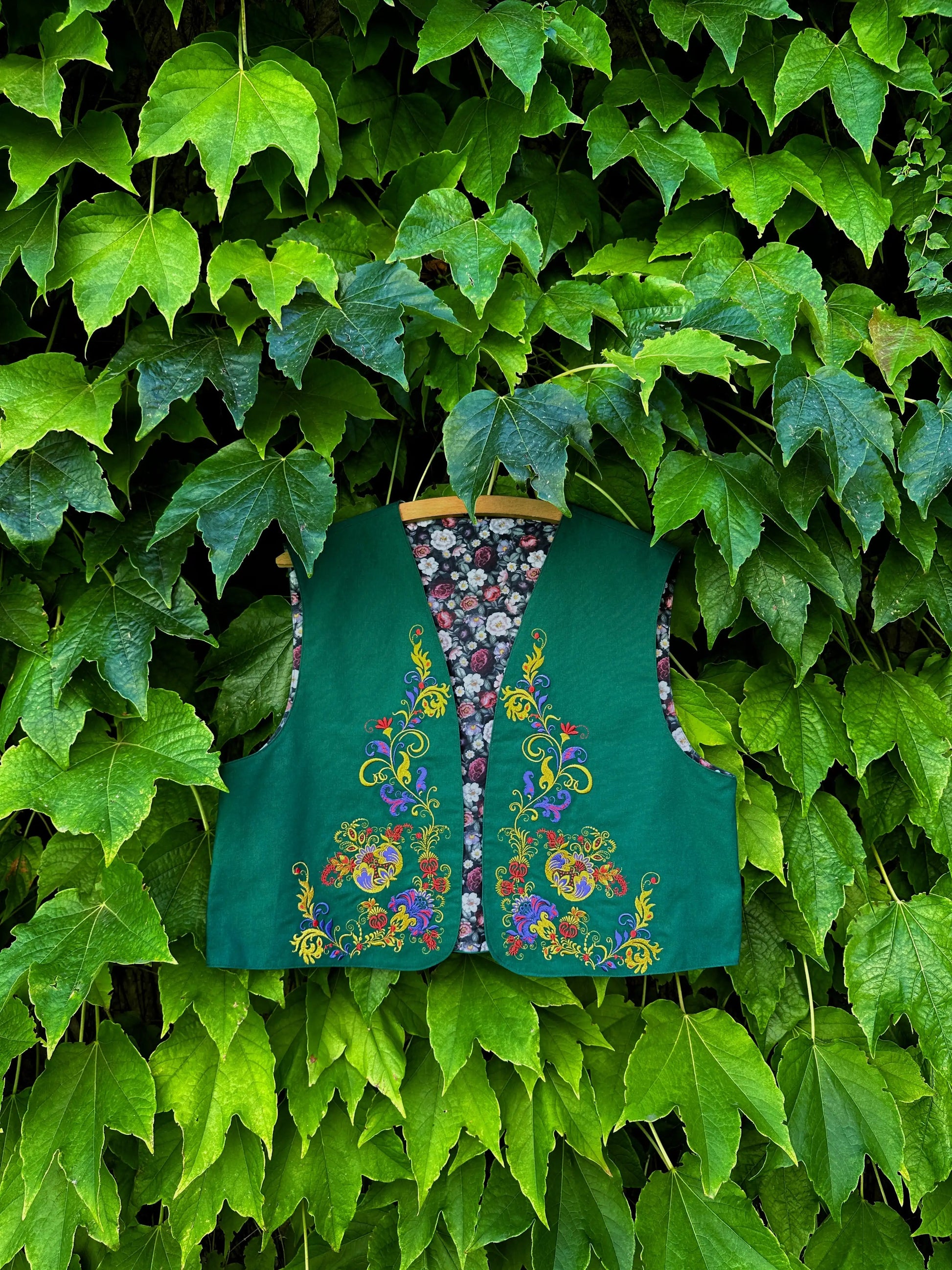 Green embroidered vest hanging against a green leafy background
