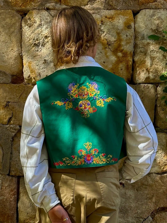 Person wearing a traditional outfit with a green vest against a stone wall.