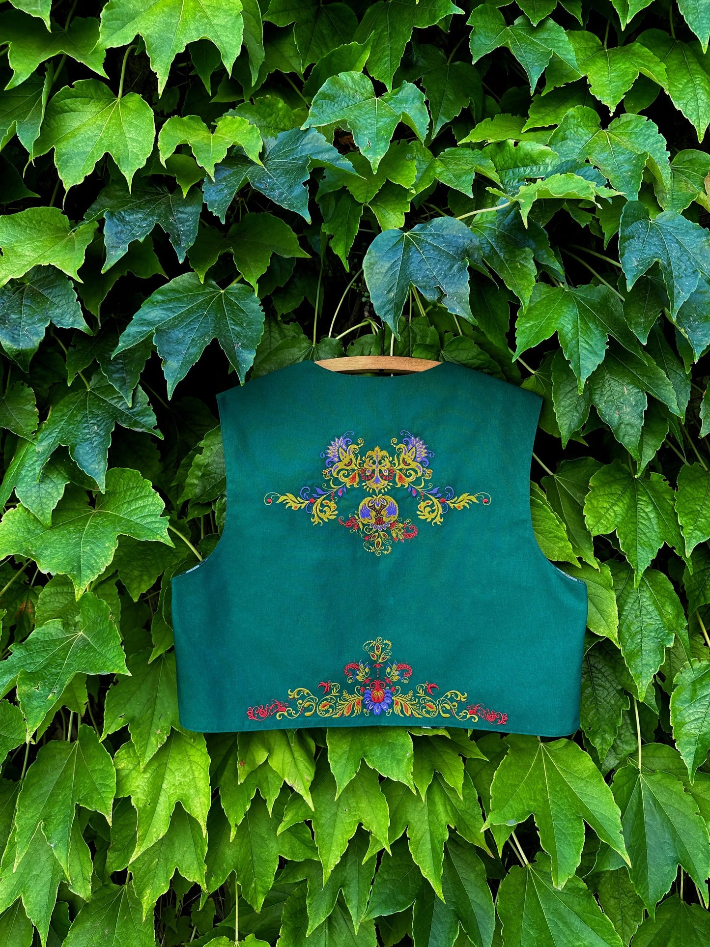 Green embroidered vest against a green leafy background