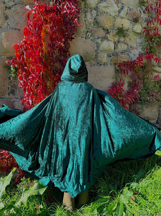 Person wearing a teal hooded cloak standing in front of a stone wall with red foliage.