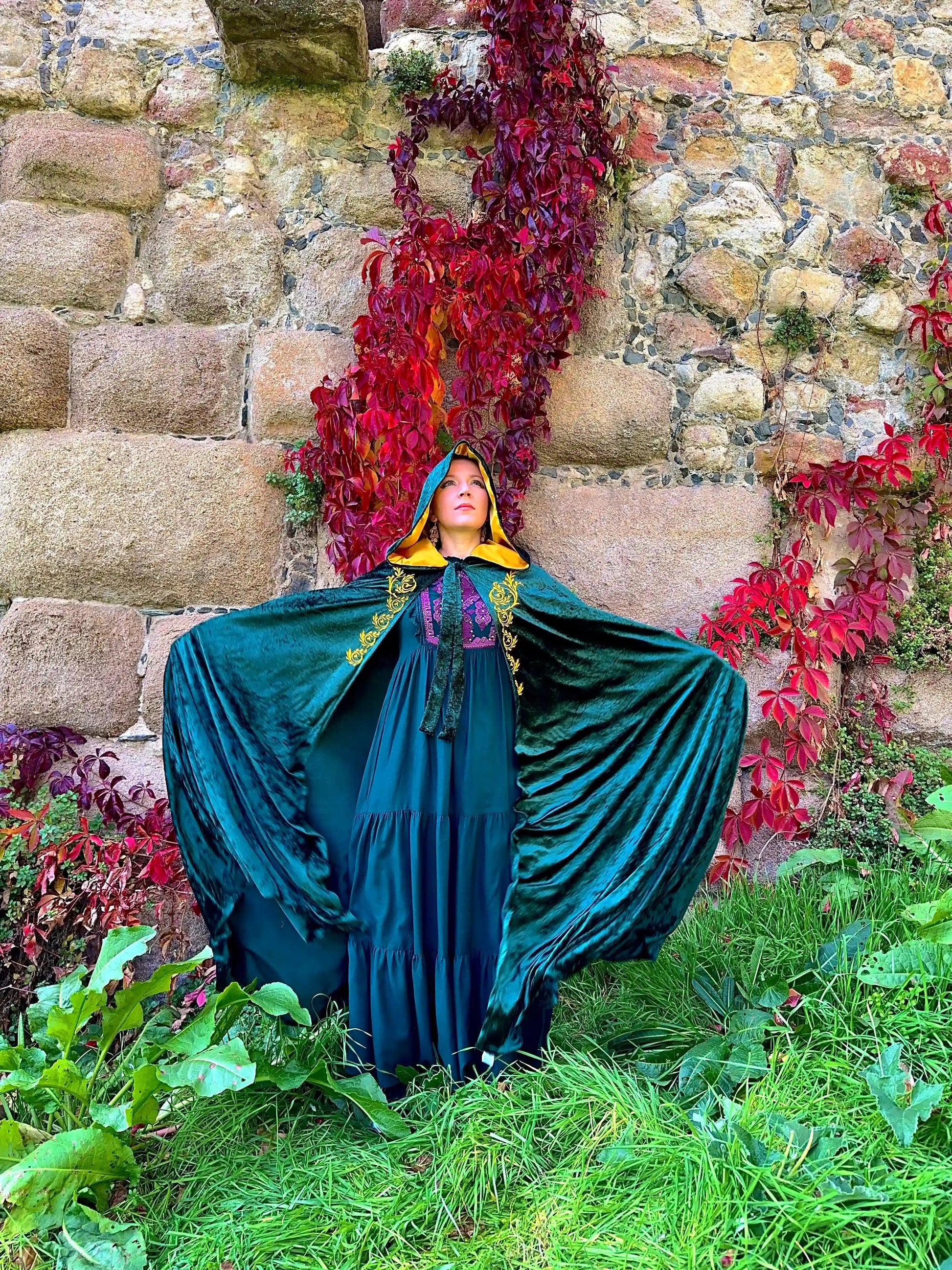 Person in a teal cloak standing in front of a stone wall with red foliage
