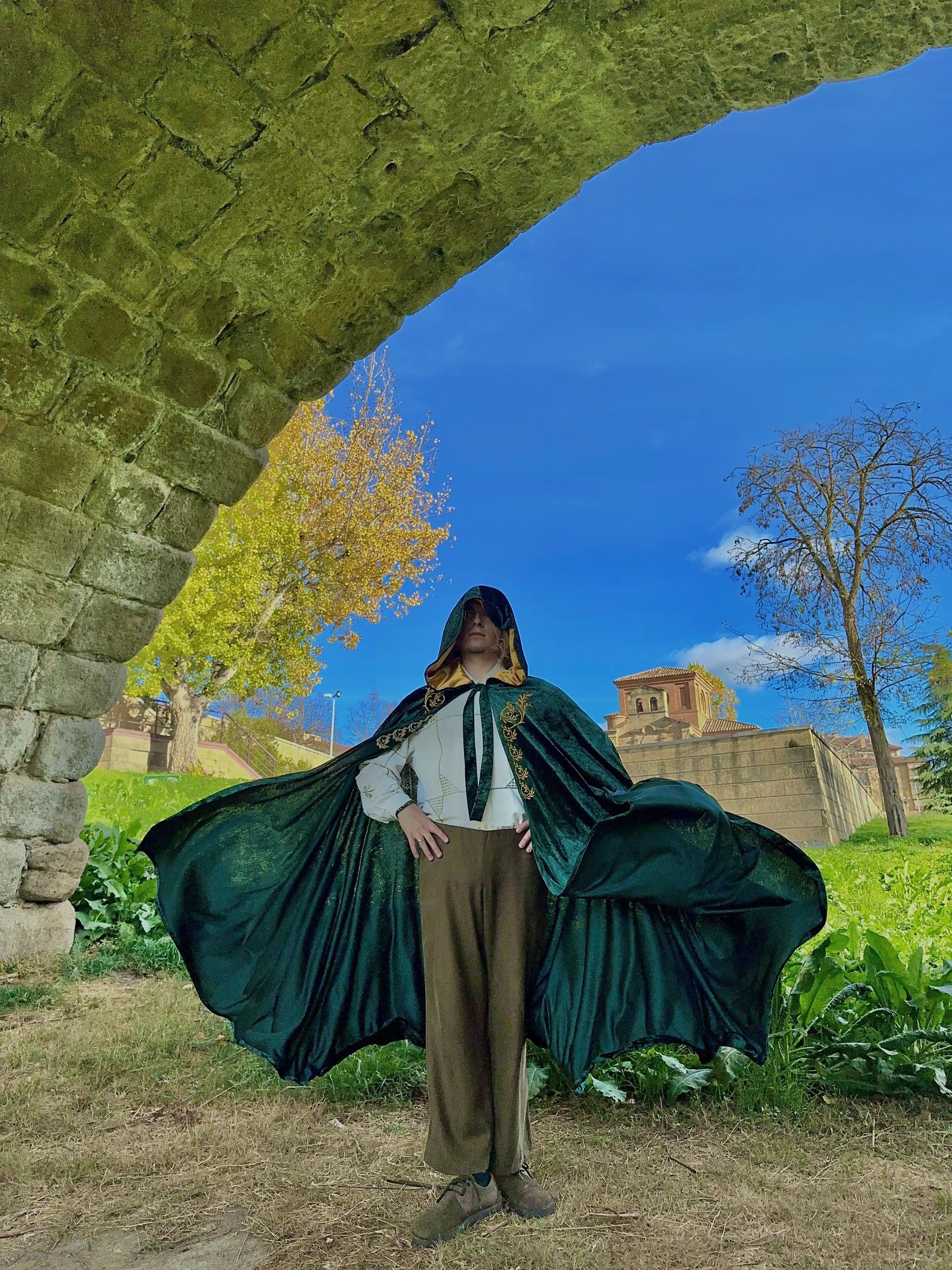 Person in a green cape standing under a stone archway with a castle in the background