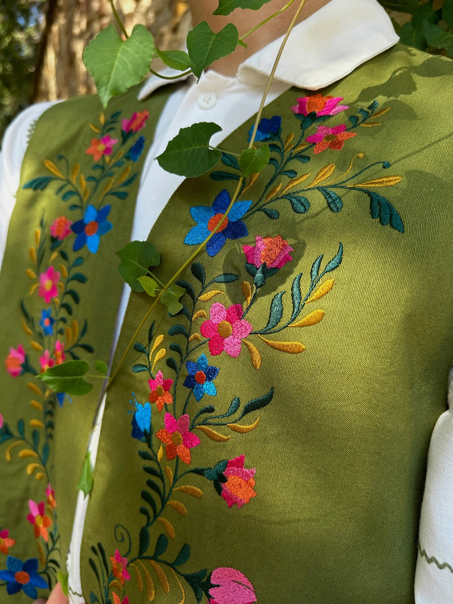 Green embroidered jacket with colorful floral patterns on a blurred natural background