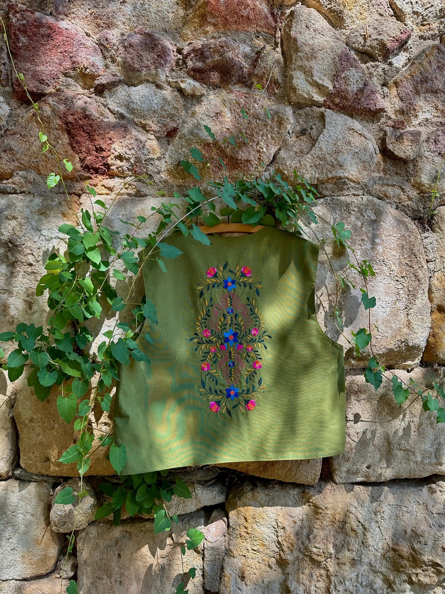 Green embroidered fabric hanging on a stone wall with greenery