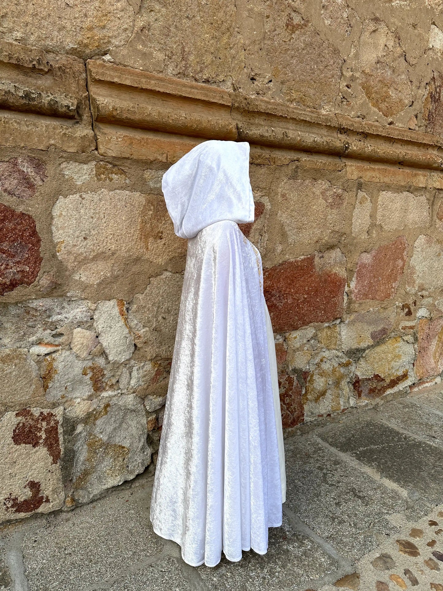 Person wearing a white hooded cloak against a stone wall.
