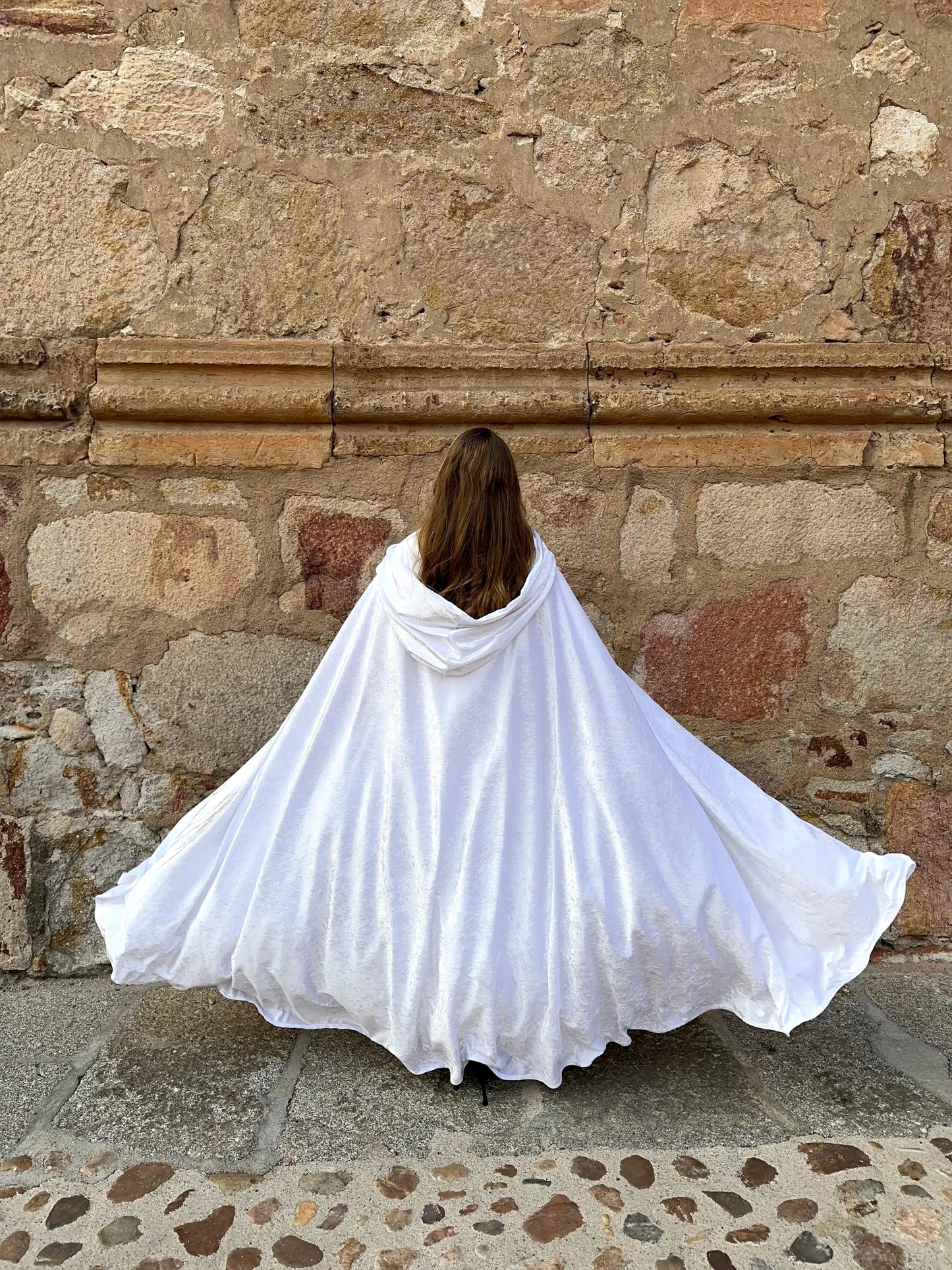 Person wearing a white cape standing against a stone wall.
