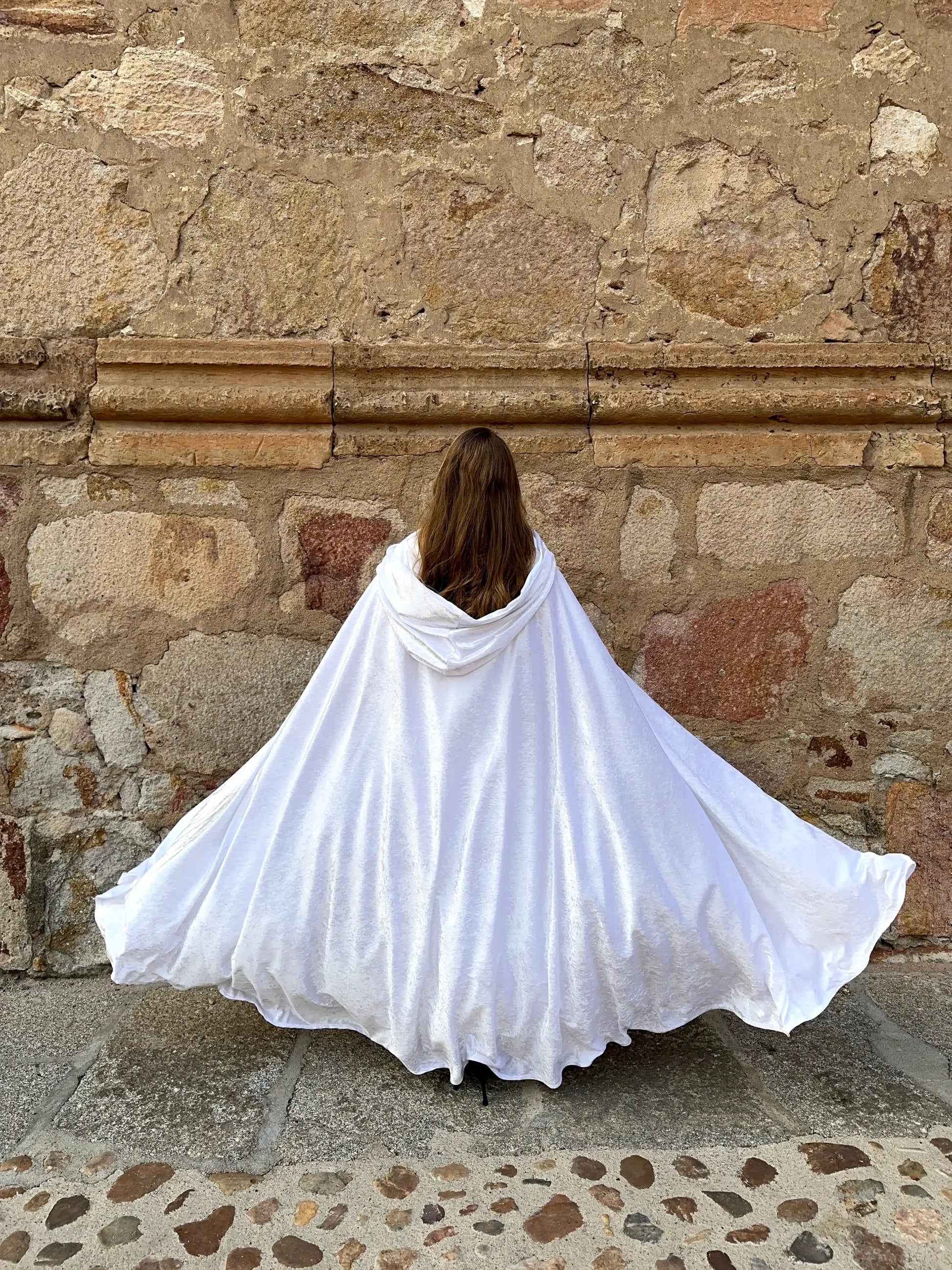 Person wearing a white cape standing against a stone wall.
