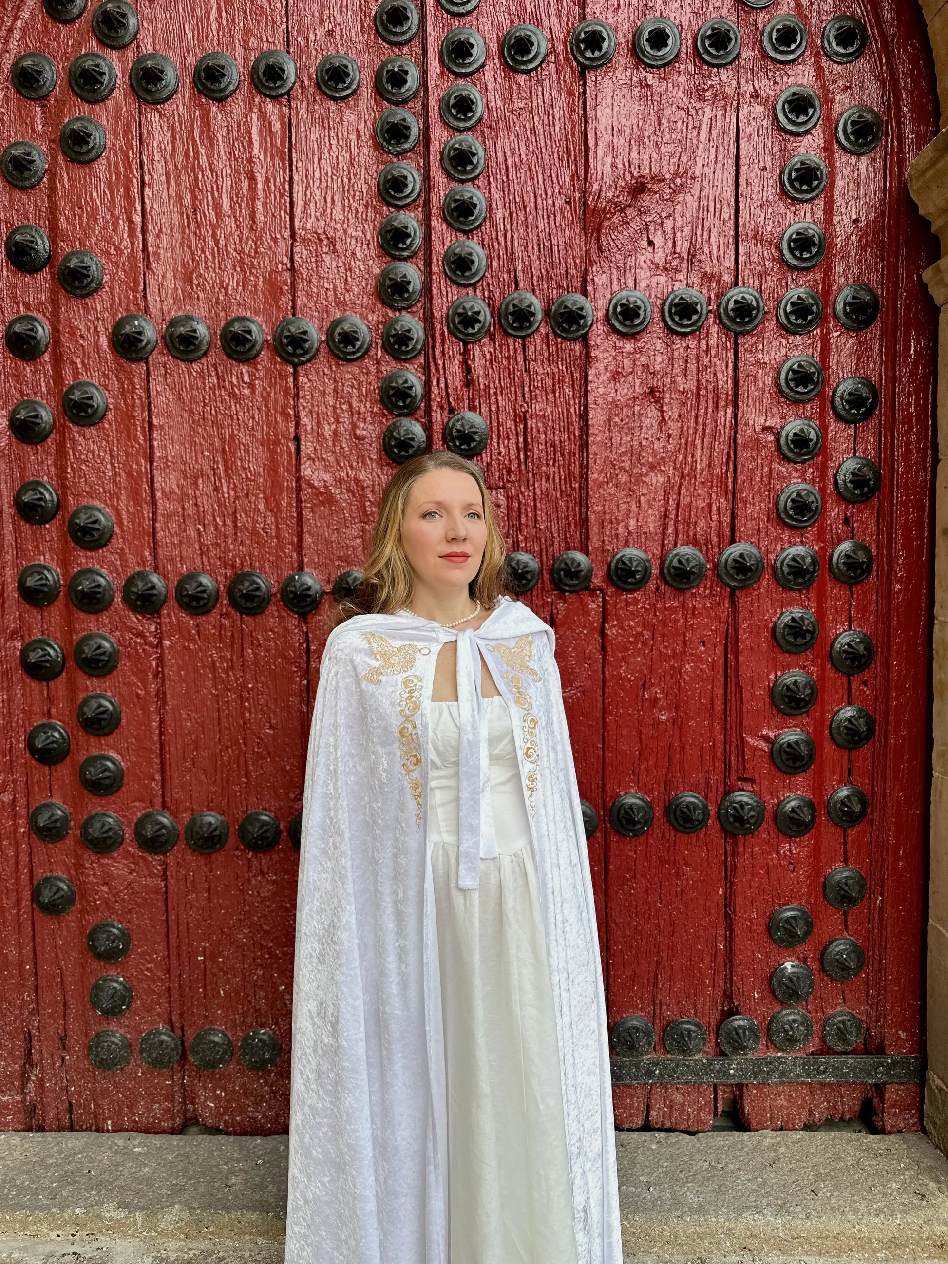 Woman in a white dress standing in front of a large red door with black metal details