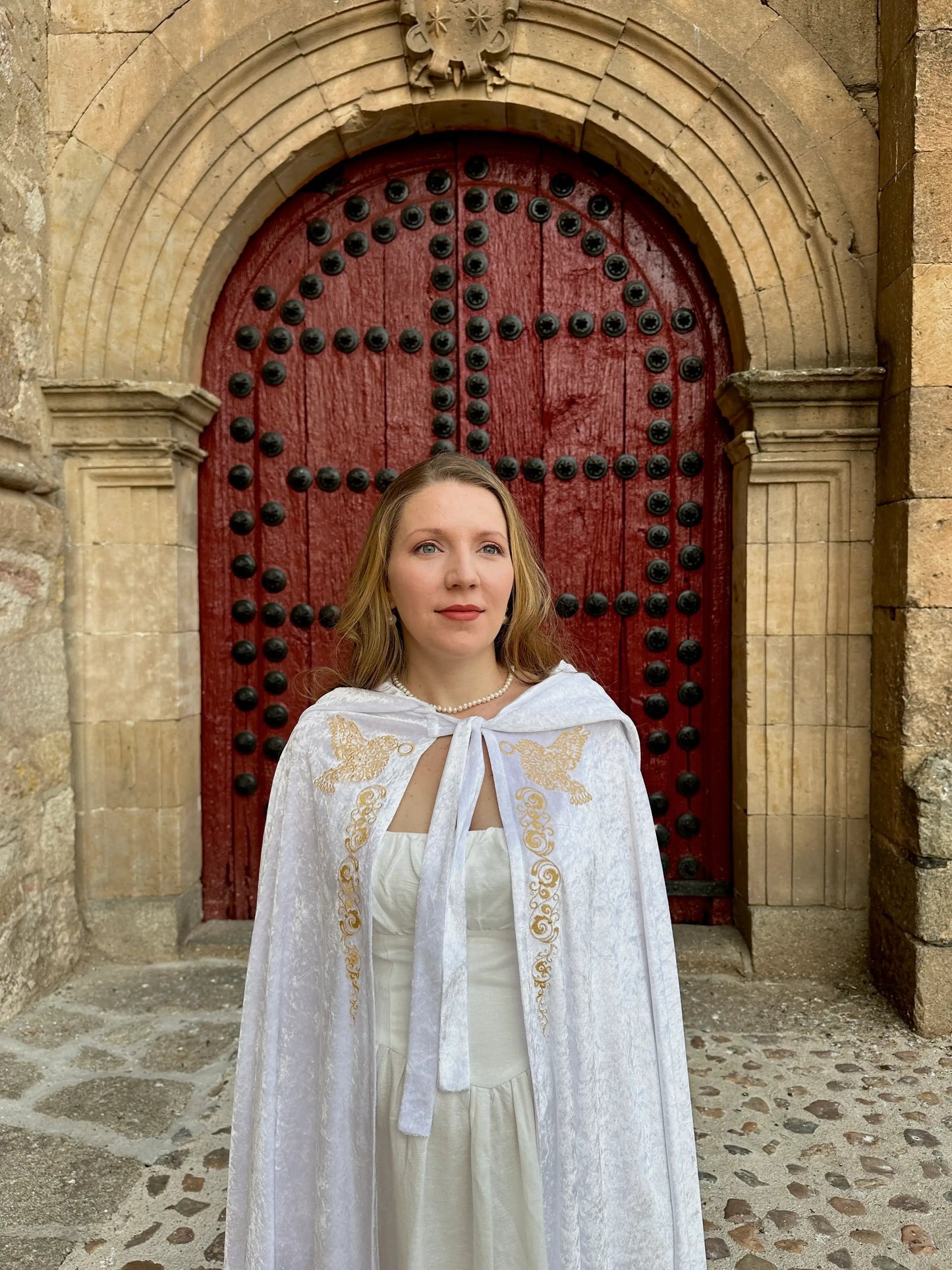 Woman in a white dress with gold embroidery standing in front of a red door.