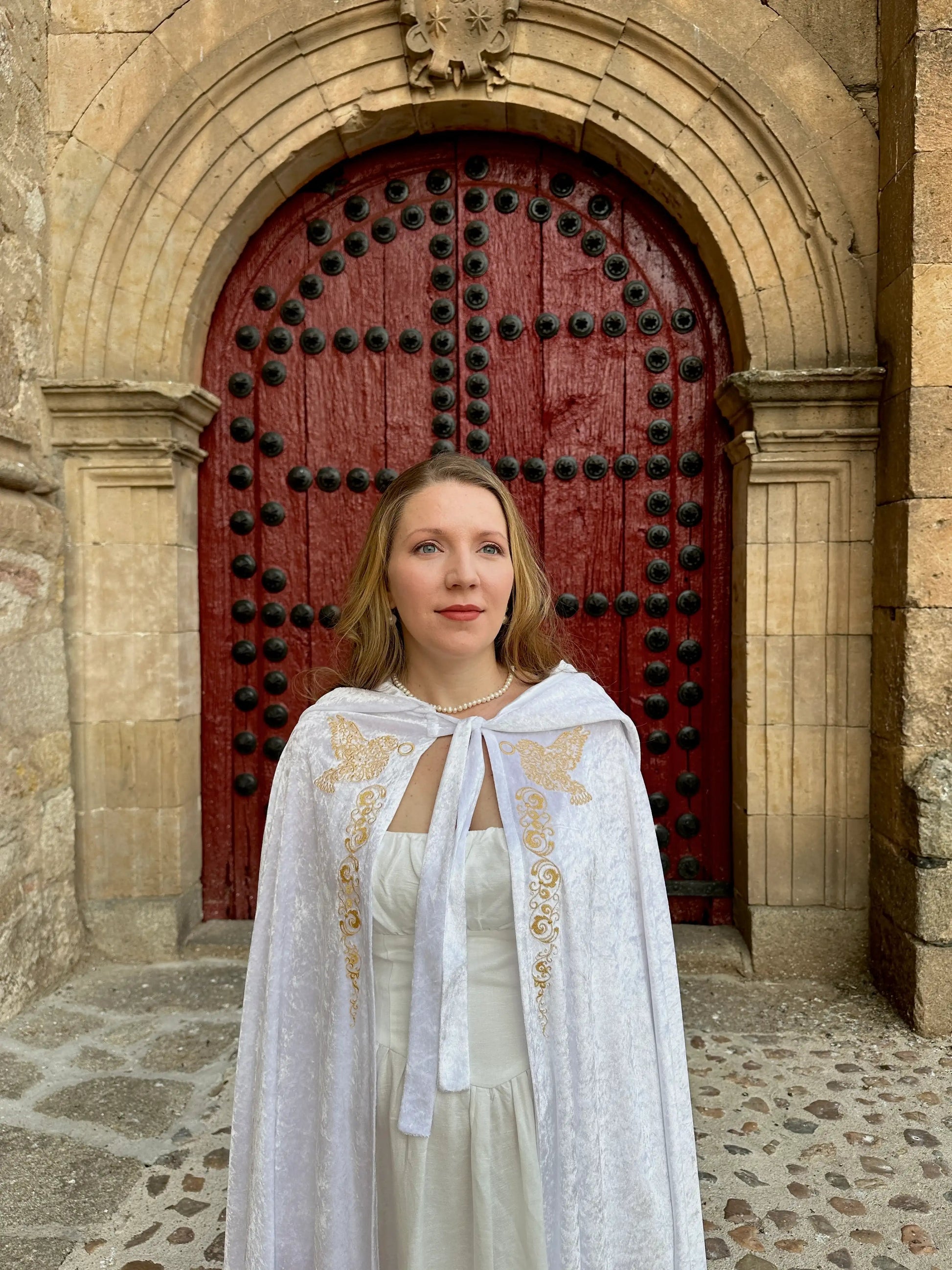Woman in a white dress with gold embroidery standing in front of a red door.
