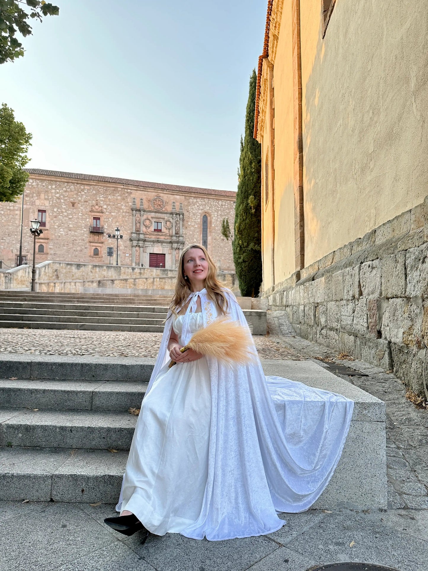 Woman in a white dress standing on stone steps with a building in the background