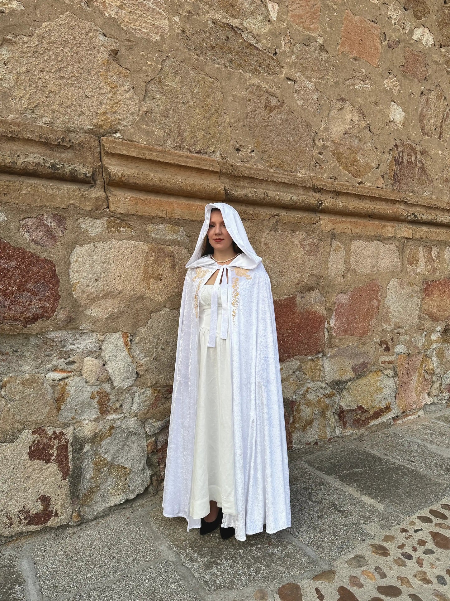 Person wearing a white cape standing against a stone wall.