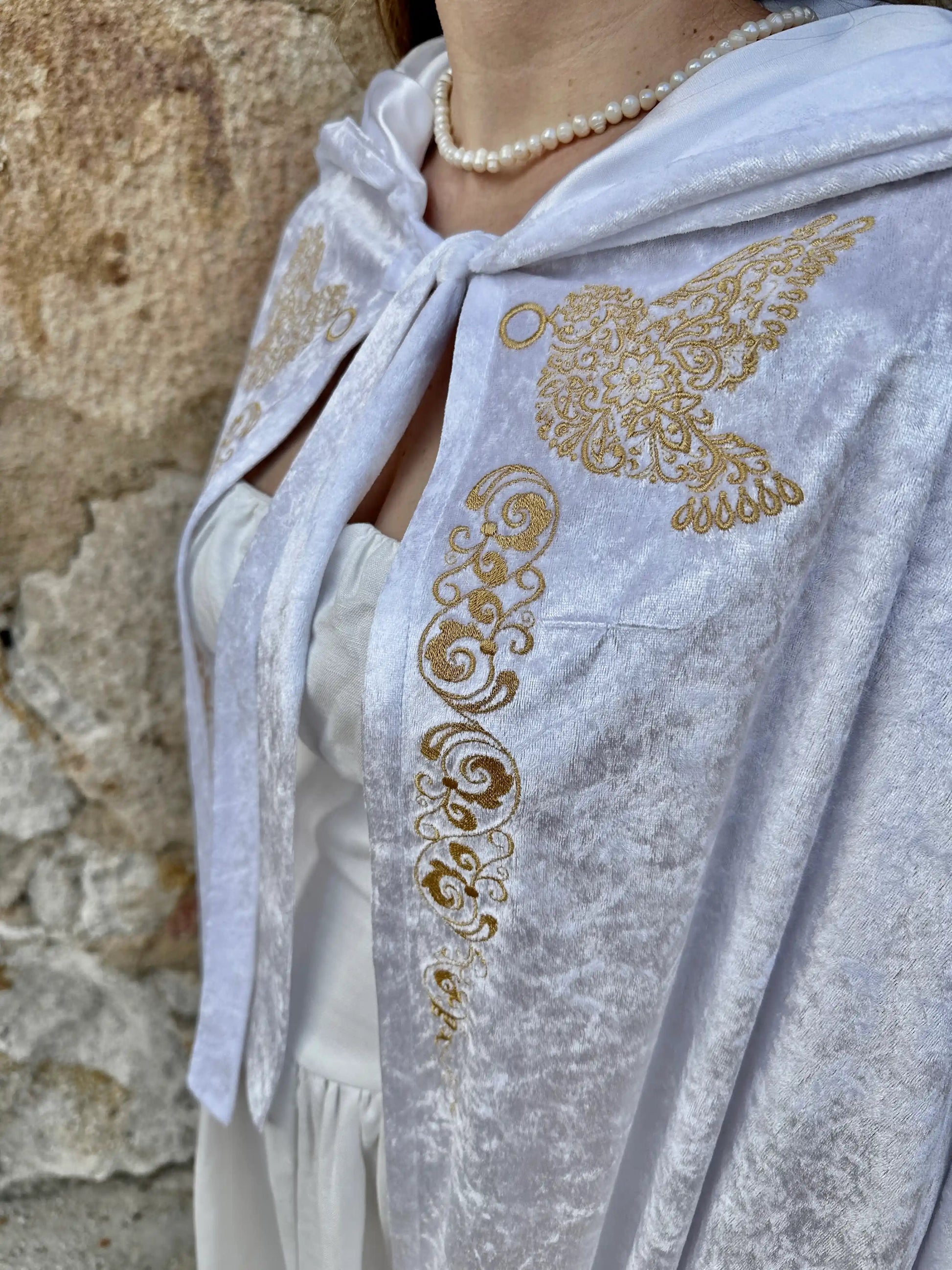 White shawl with gold embroidery draped over a person against a stone wall.