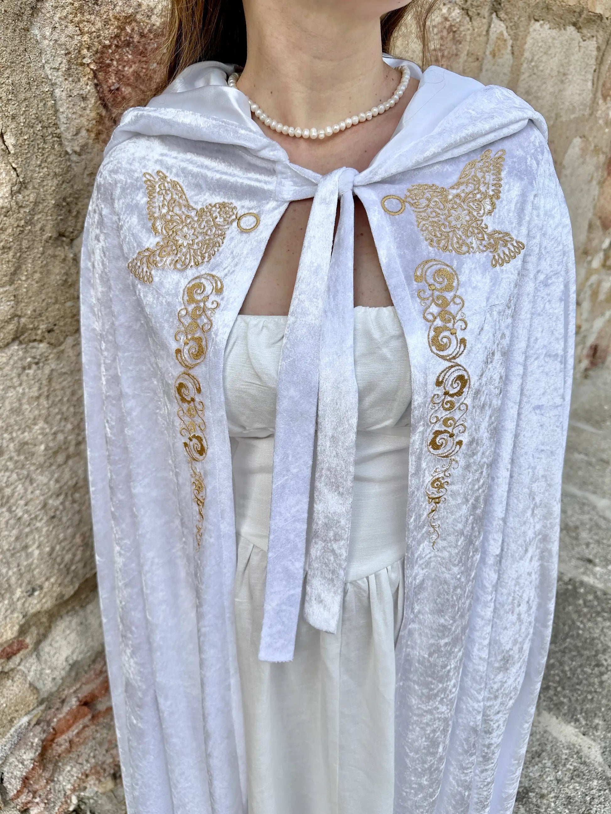 White embroidered shawl with gold butterflies worn by a person against a stone wall.