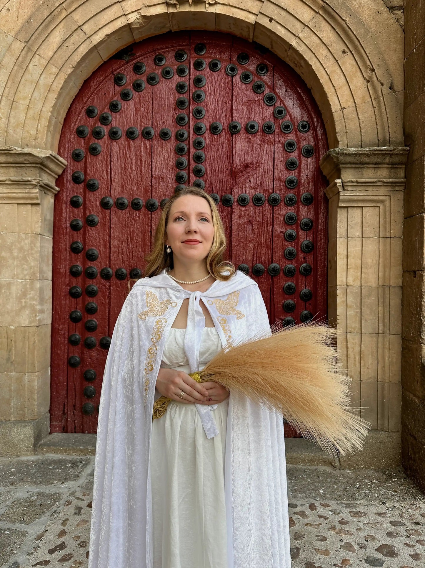Woman in a white dress with a long braid standing in front of a large red door.