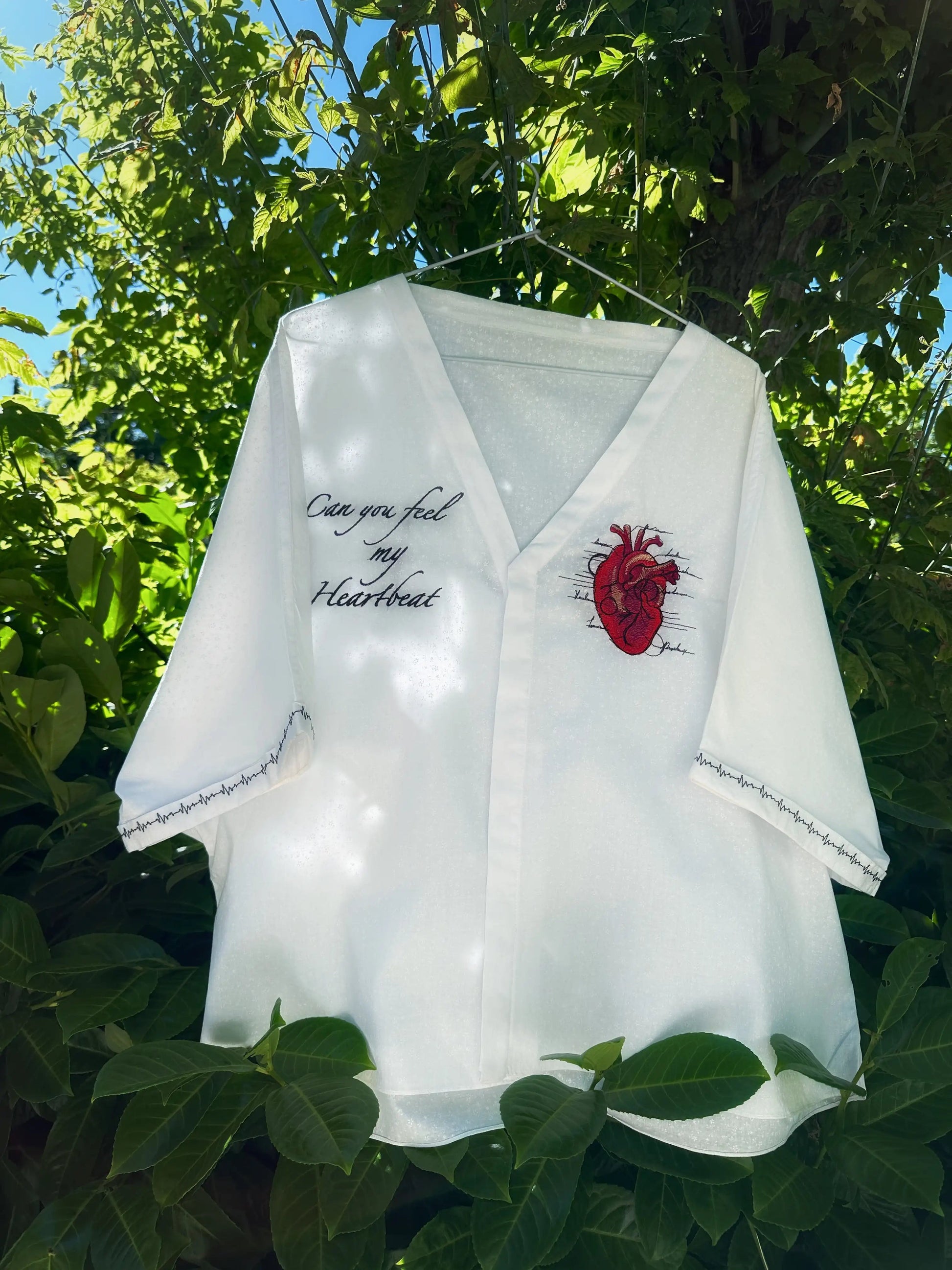 White shirt with red heart design and text hanging outdoors among green leaves