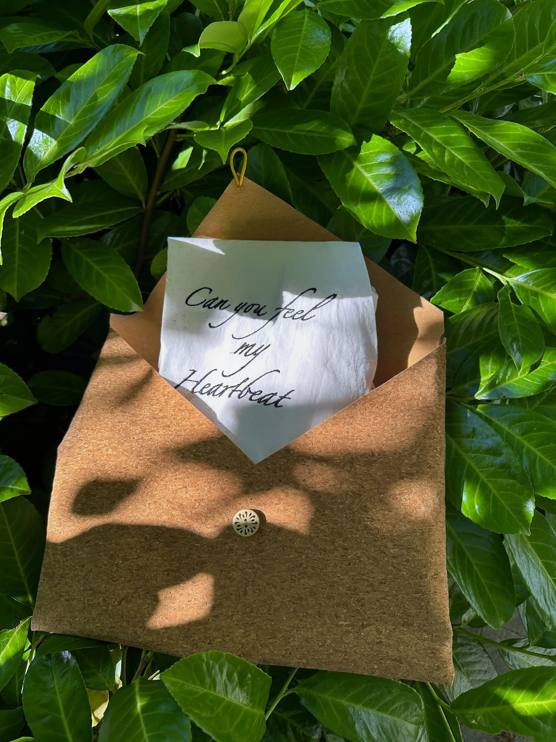 Brown envelope with a white card inside, hanging on green leaves
