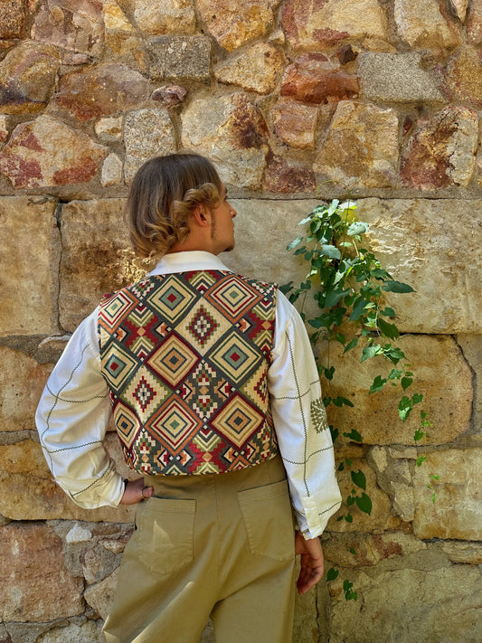 Person wearing a patterned vest against a stone wall