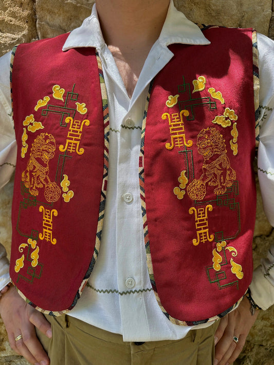 Red embroidered vest over a white shirt with a stone wall background