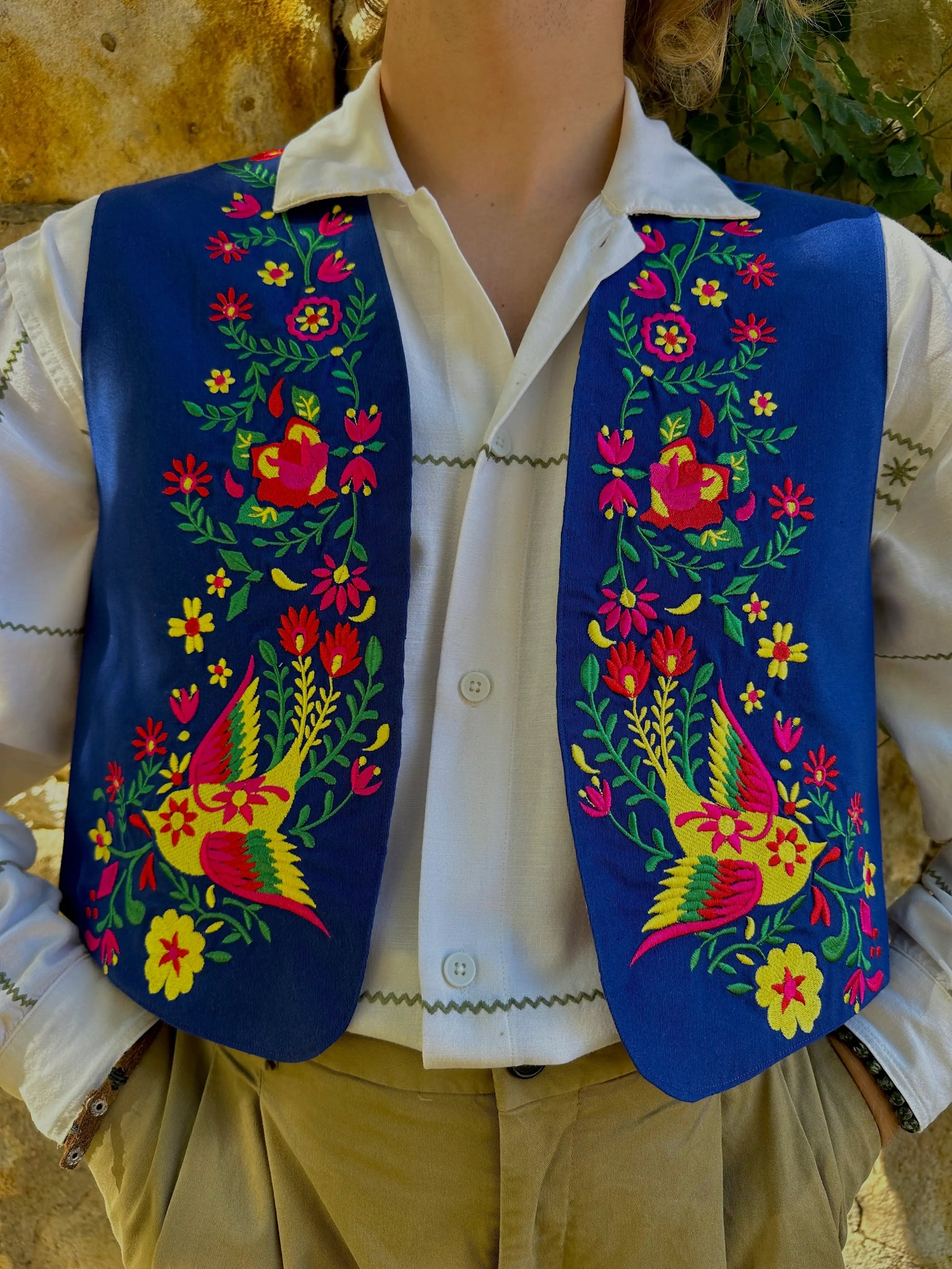Person wearing a colorful embroidered vest over a white shirt with a natural background
