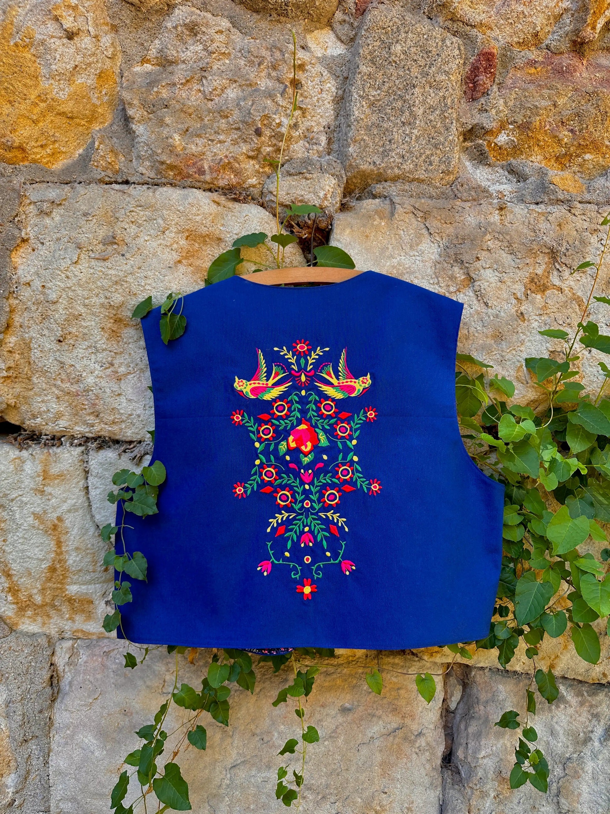 Blue embroidered vest against a stone wall with greenery