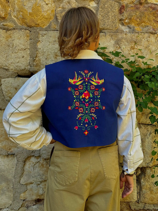 Person wearing a blue embroidered vest against a stone wall