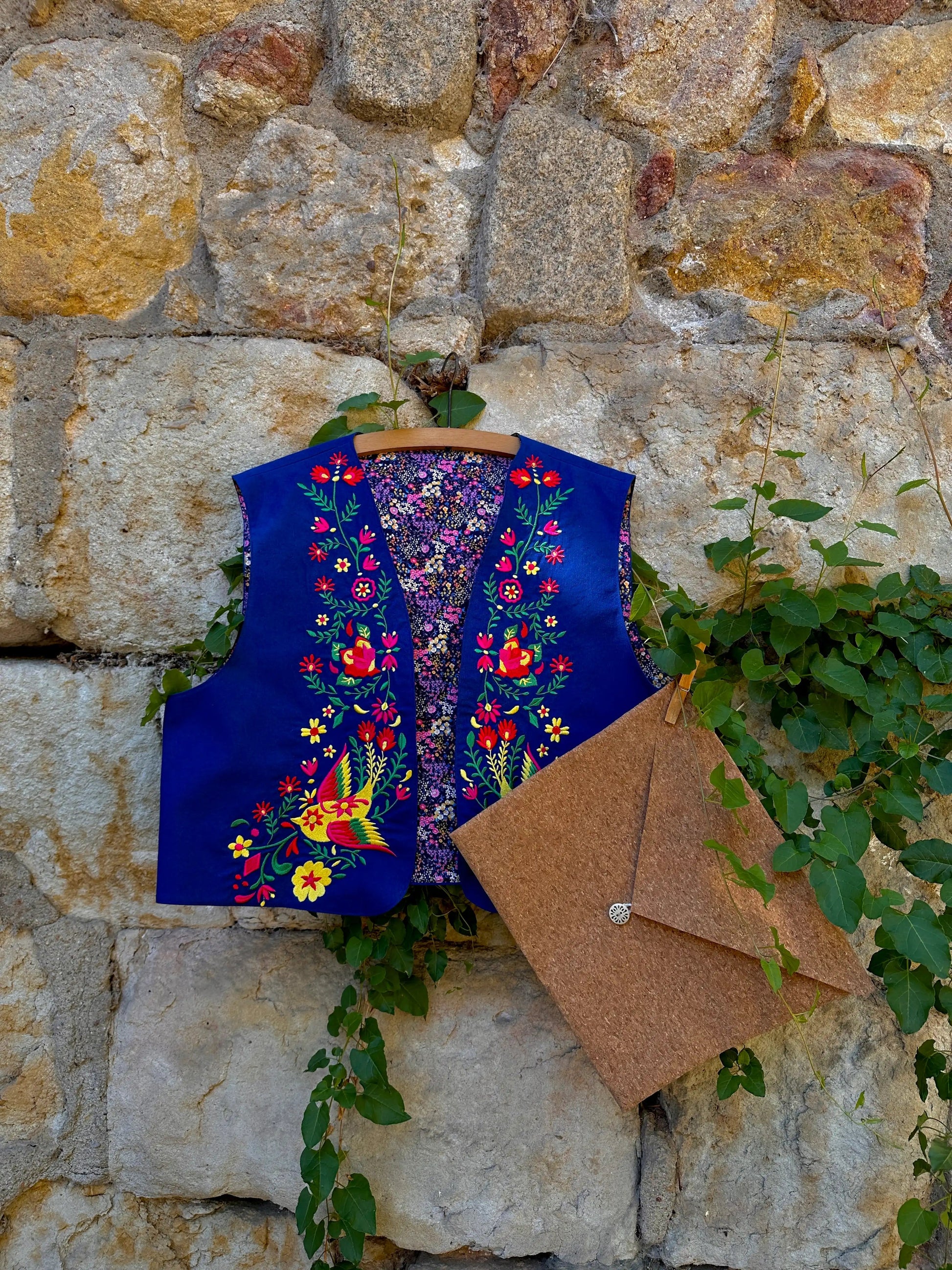 Embroidered blue vest with floral patterns on a stone wall