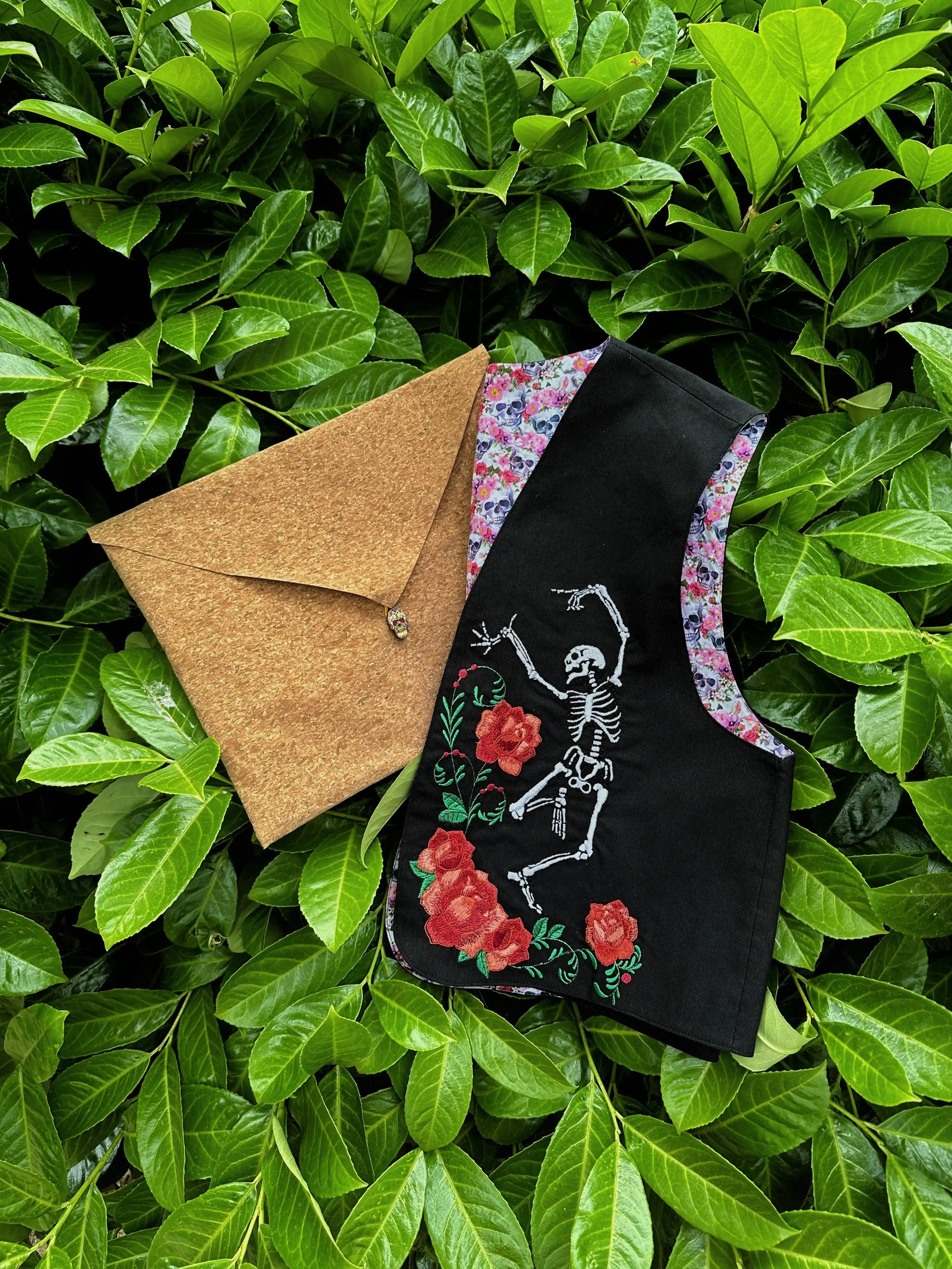 Brown envelope and black embroidered bag with skeleton and roses design on green leaves