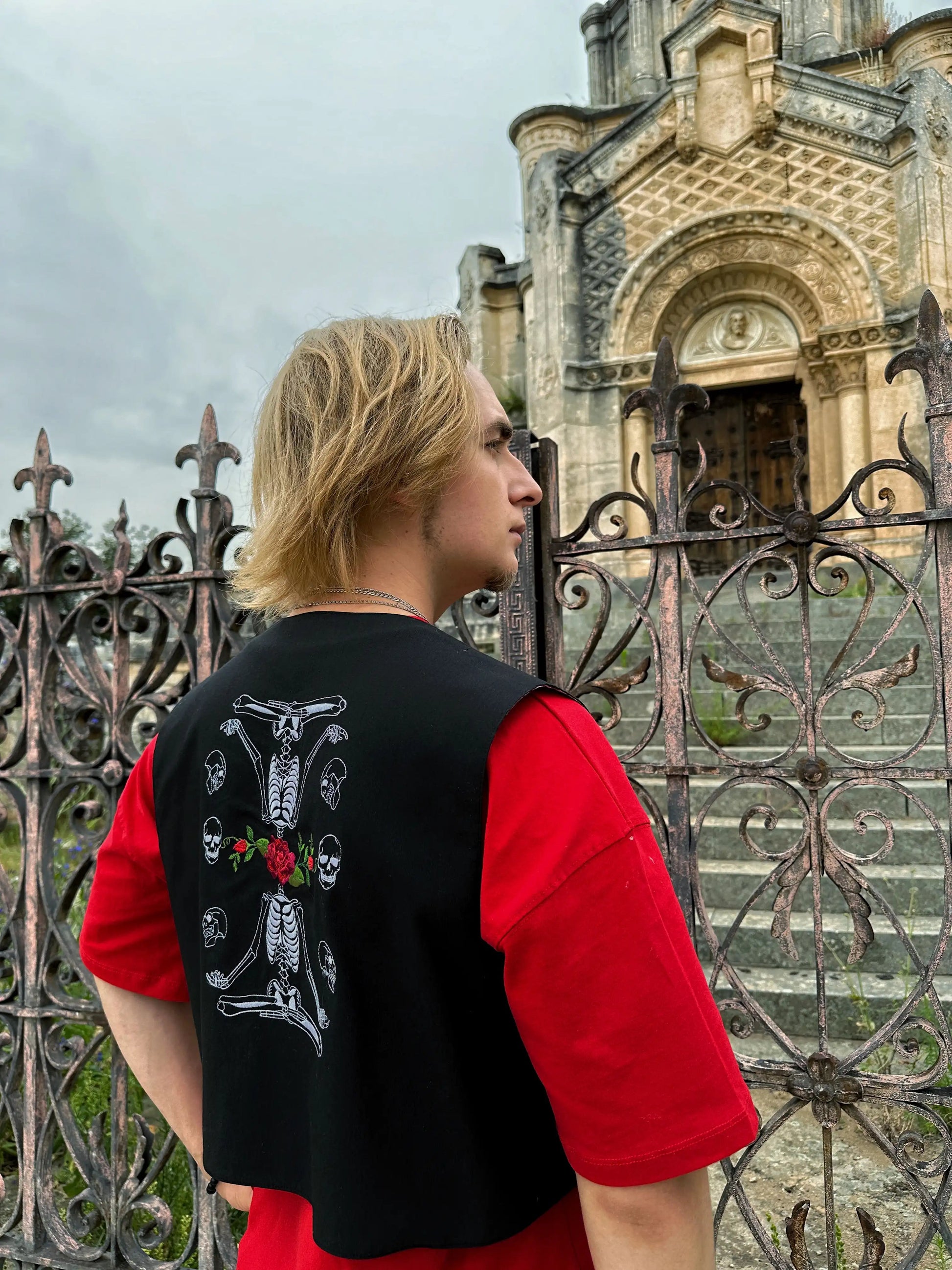 Person wearing a black jacket with a design on the back, standing in front of an ornate building.