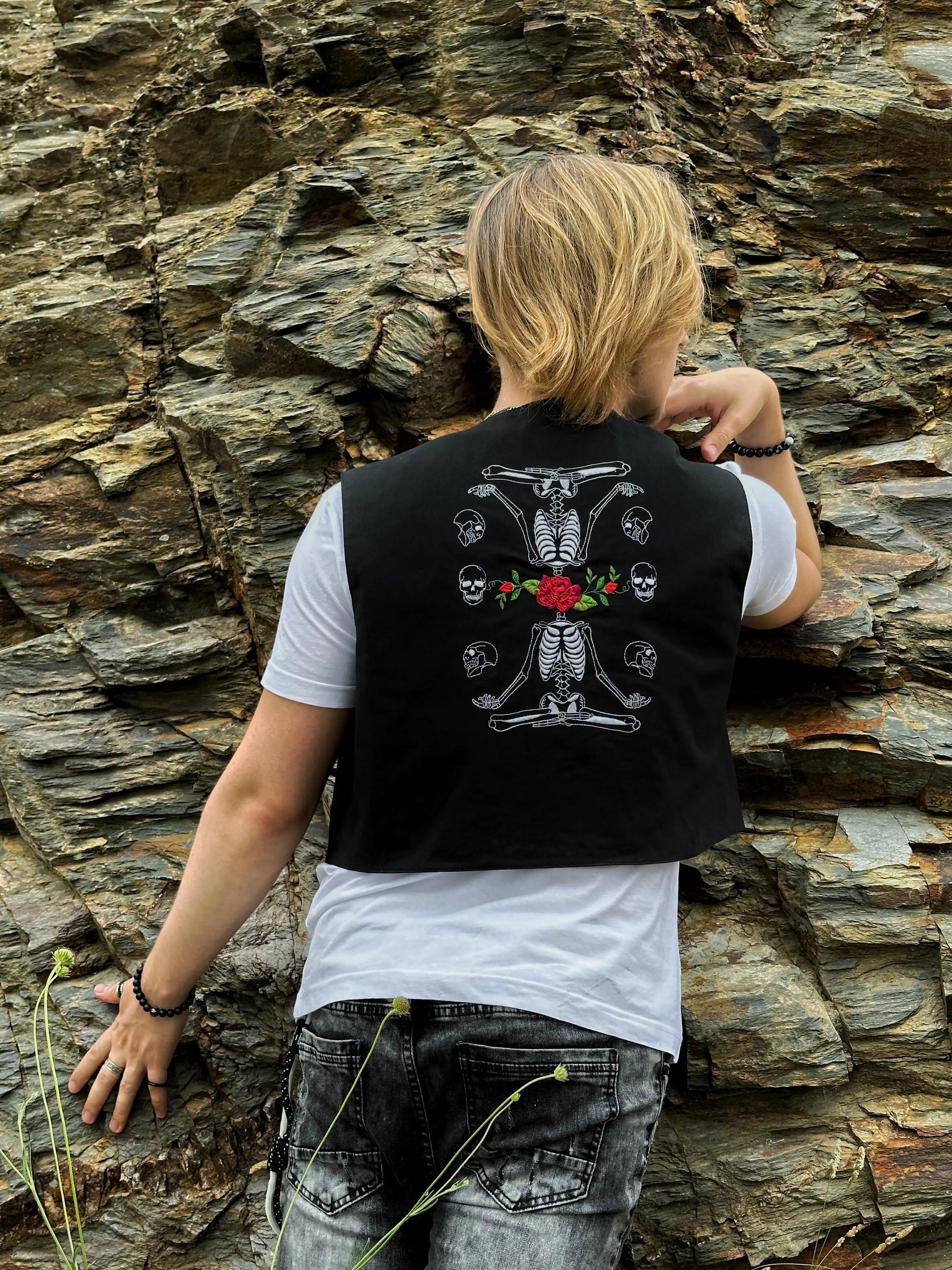 Person wearing a black vest with a skeleton design against a stone wall.