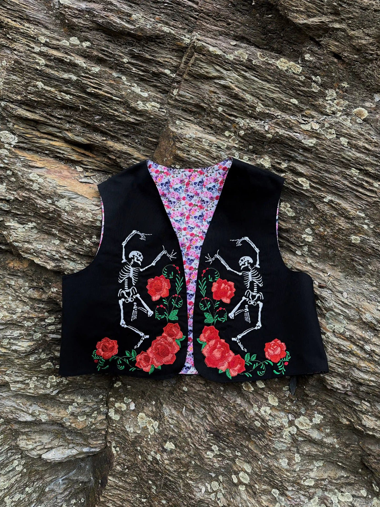 Black vest with skeleton and rose design on a wooden surface