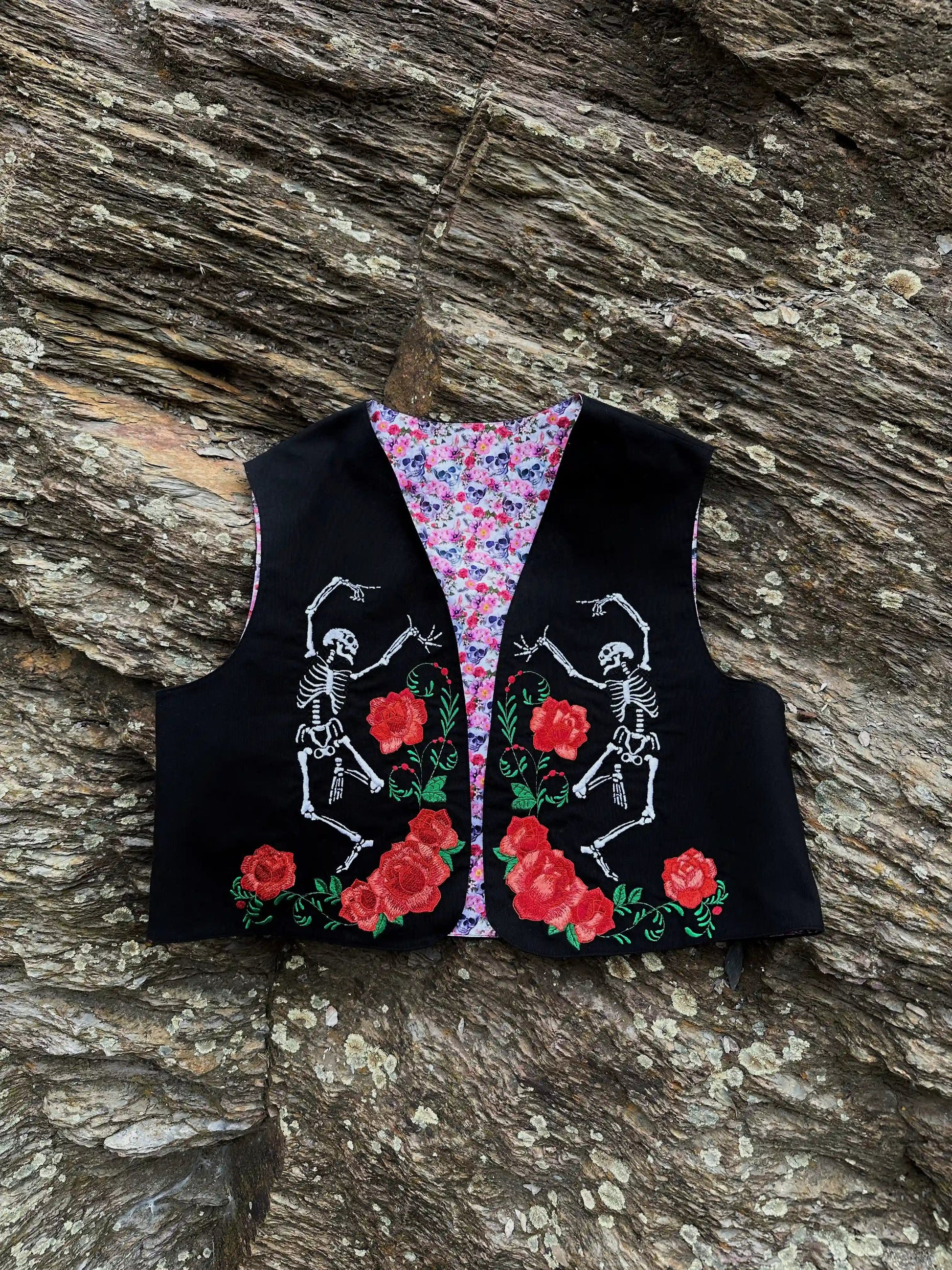 Black vest with skeleton and rose design on a wooden surface