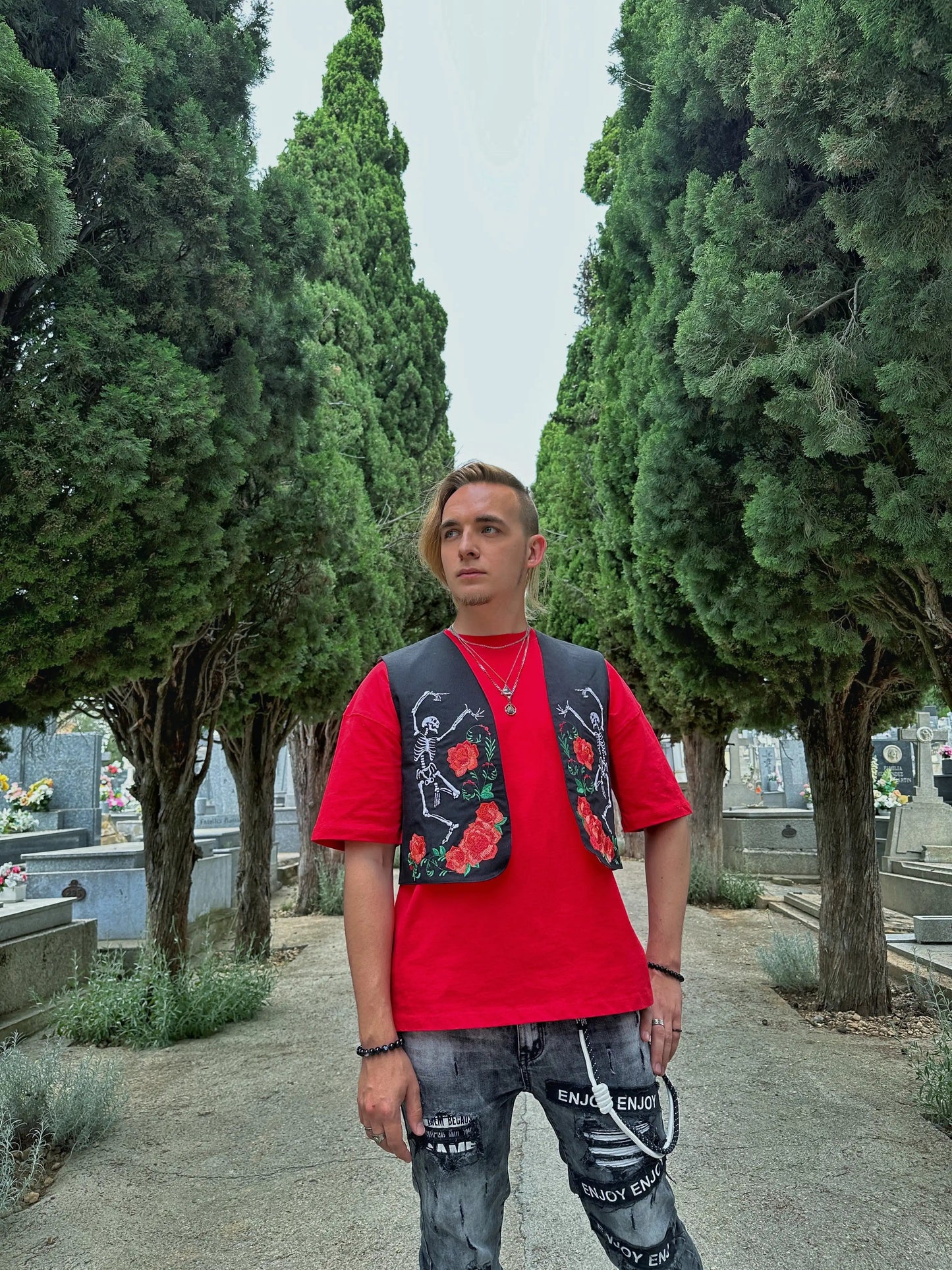 Person wearing a red shirt and floral vest standing in a cemetery.