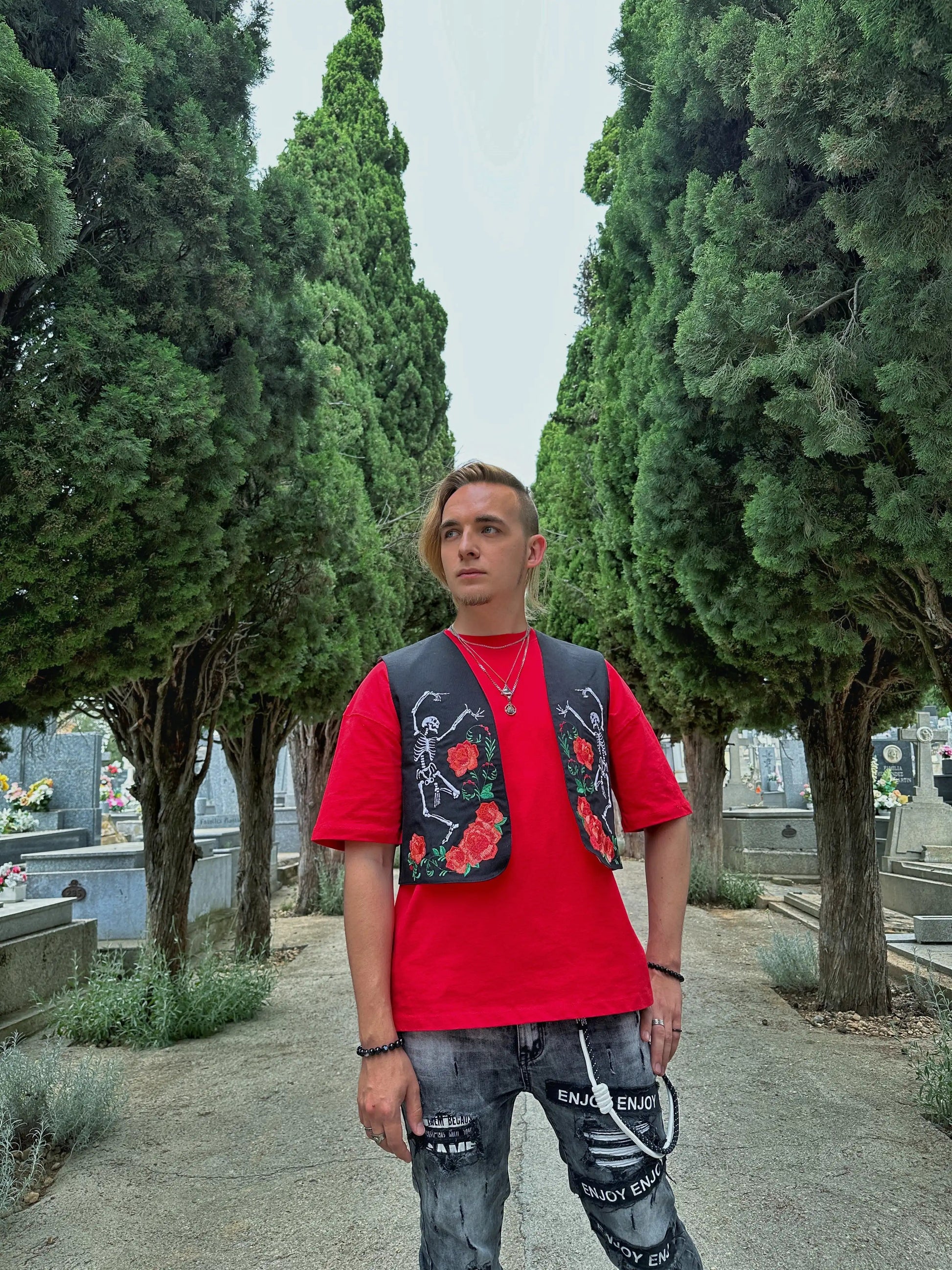 Person wearing a red shirt and floral vest standing in a cemetery.