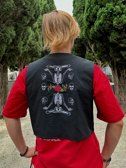 Person wearing a black vest with skeleton design in a cemetery