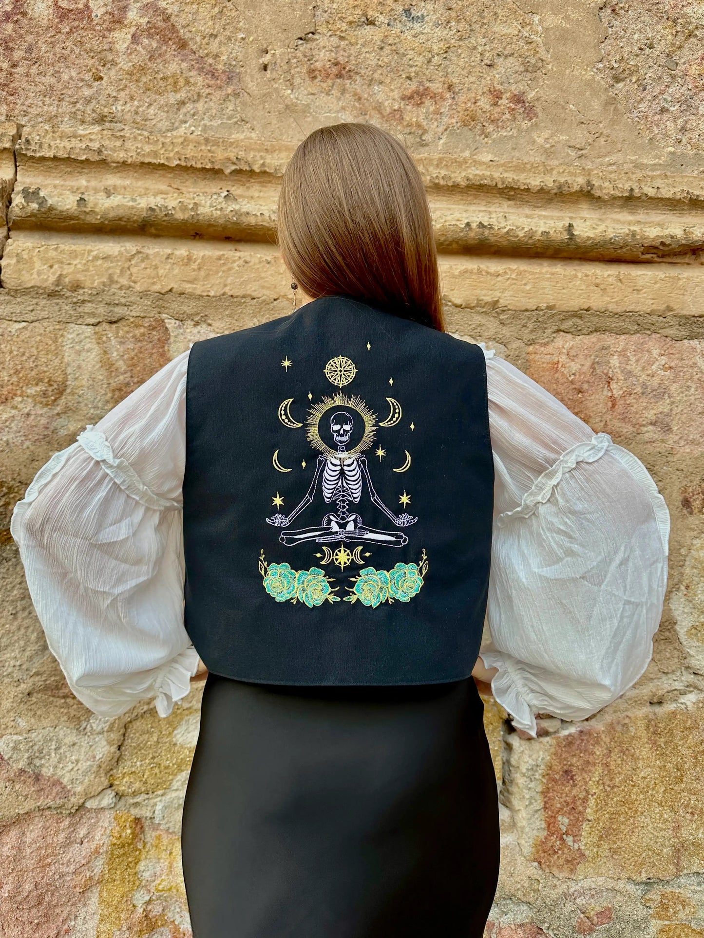 Person wearing a black vest with a skeleton design against a stone wall.
