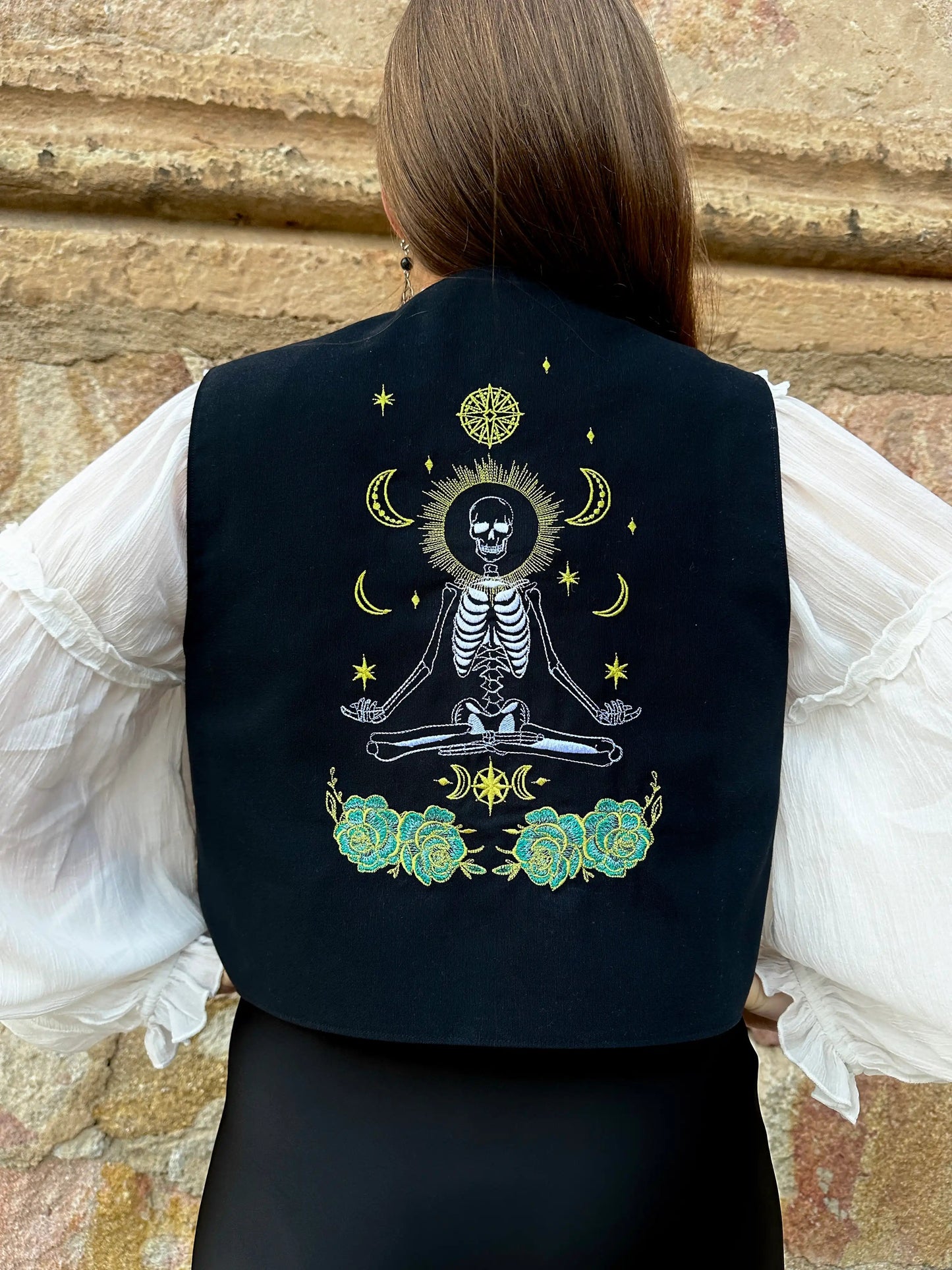 Person wearing a black vest with a skeleton design against a stone wall background