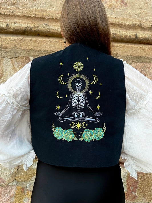 Person wearing a black vest with a skeleton design against a stone wall background